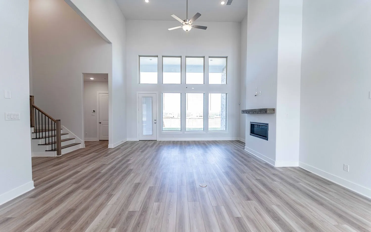 Spacious living area featuring wood-finish flooring, a two-story ceiling, and a modern fireplace with a distressed wood mantel