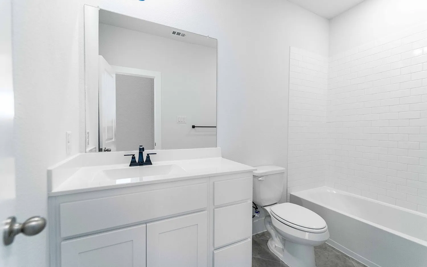 Bathroom featuring a white vanity with integrated sink, a rectangular mirror, a toilet, a bathtub, and white subway tile surround
