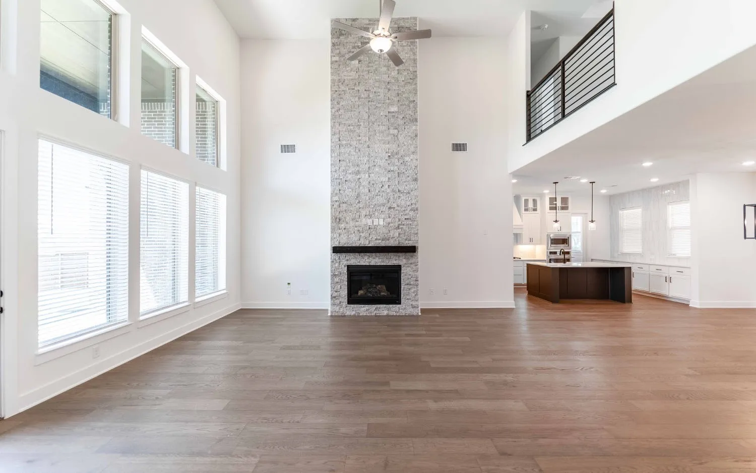 Vaulted living space featuring wood-finish flooring, a floor-to-ceiling stone fireplace with a dark wood mantel, and expansive windows