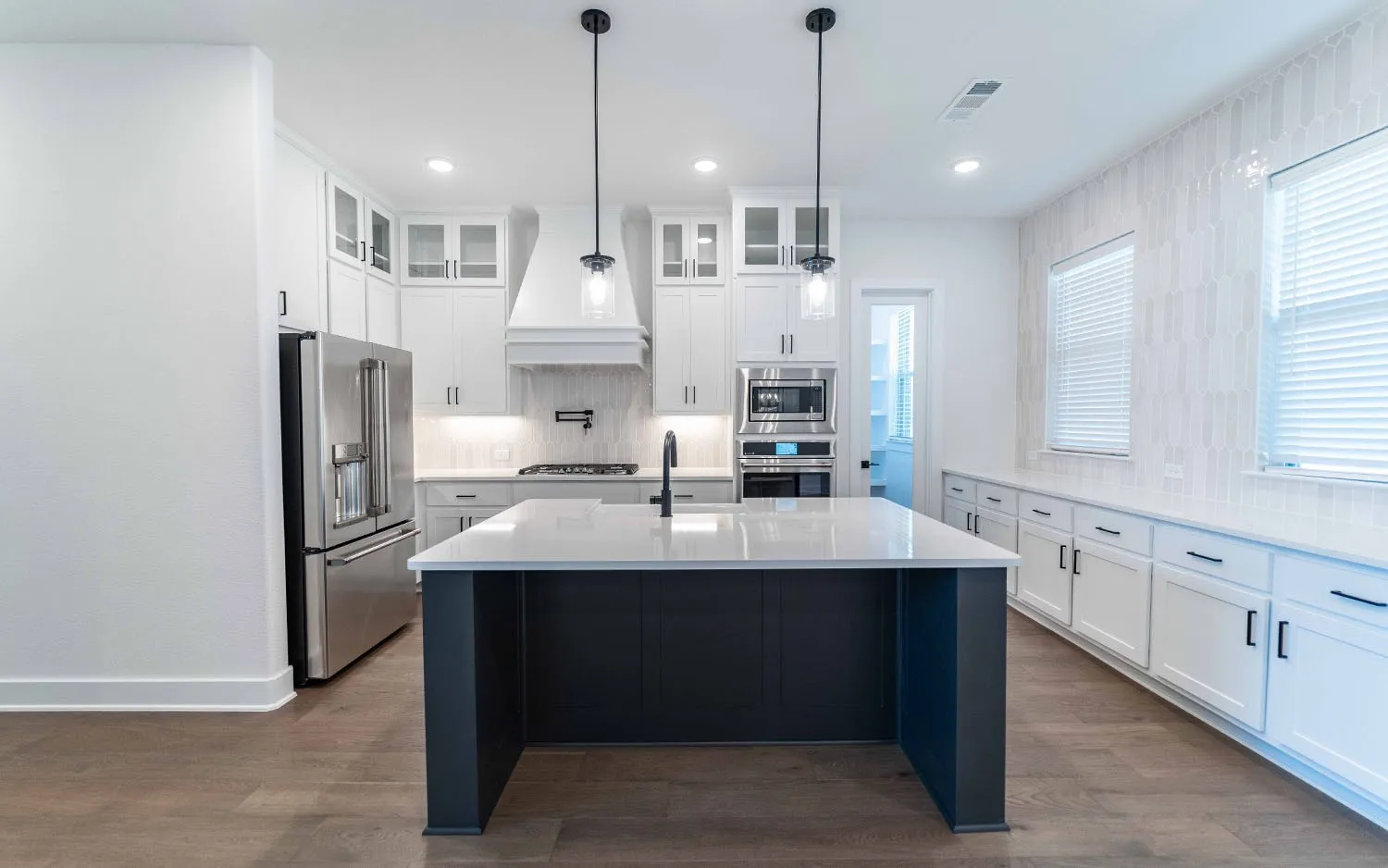 Gourmet kitchen featuring a large central island, white cabinetry, stainless steel appliances, wood-finish flooring, and pendant lighting