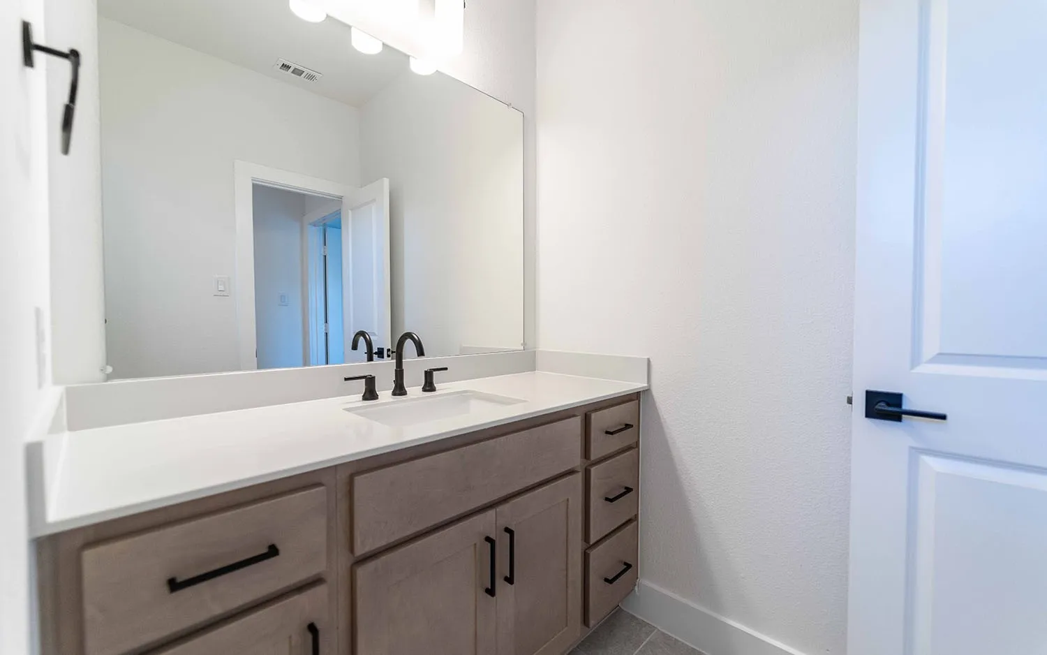 Bathroom vanity featuring a light wood-finish cabinet with black hardware, an integrated white sink, and a white countertop