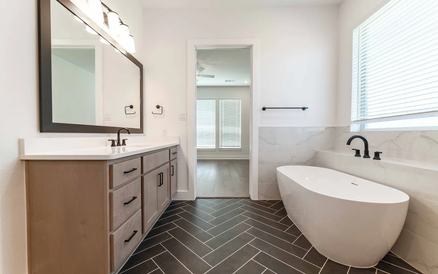 Bathroom featuring a freestanding tub, dual vanity with undermount sinks, quartz countertop, dark wood-finish cabinetry, and herringbone tile flooring