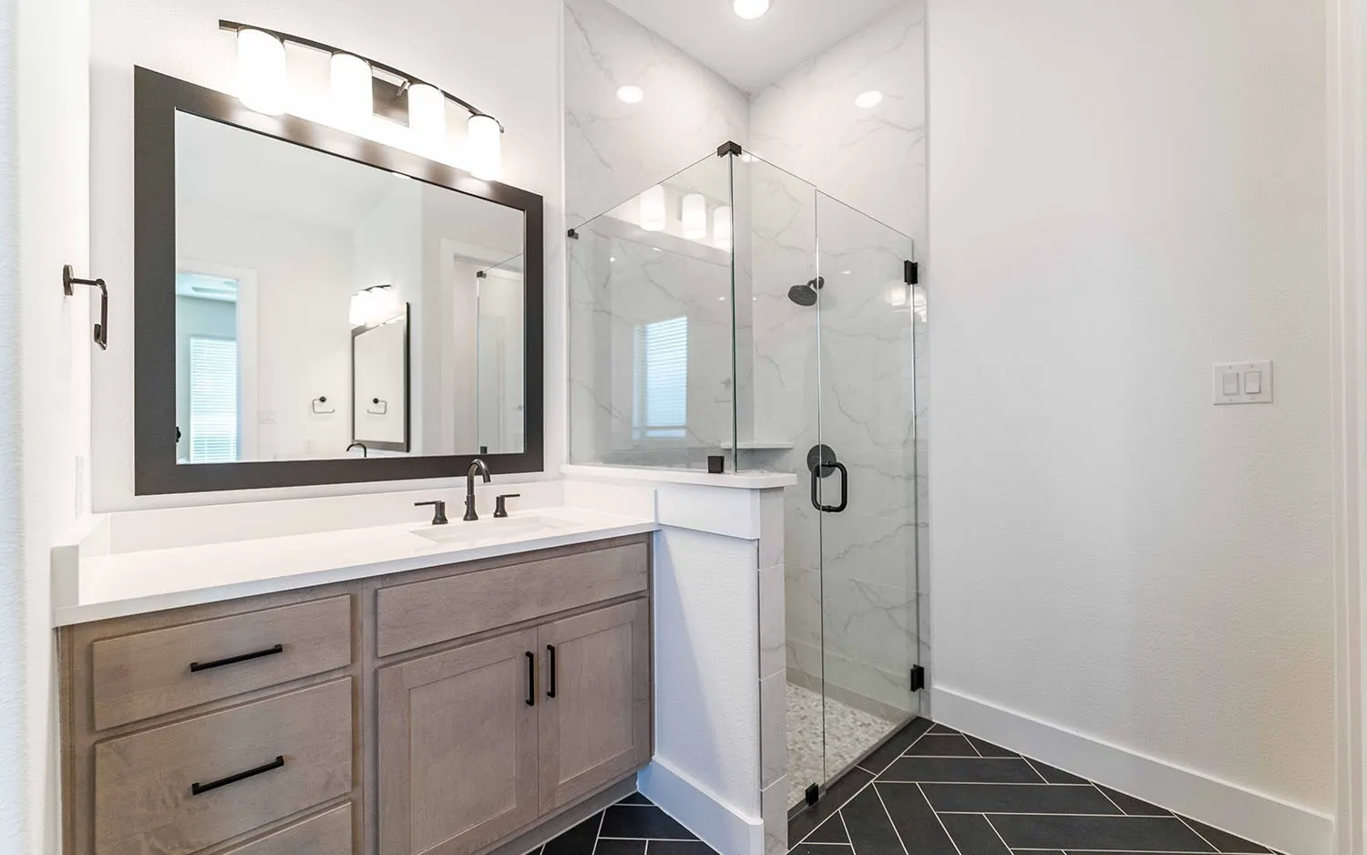 Modern bathroom with a glass-enclosed shower featuring a dark showerhead and handle, and a stone-tiled floor