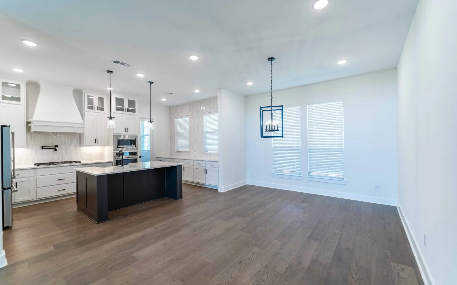 Spacious kitchen and dining area featuring wood-finish flooring, white cabinetry, a large kitchen island with a dark base, stainless steel appliances, and recessed lighting