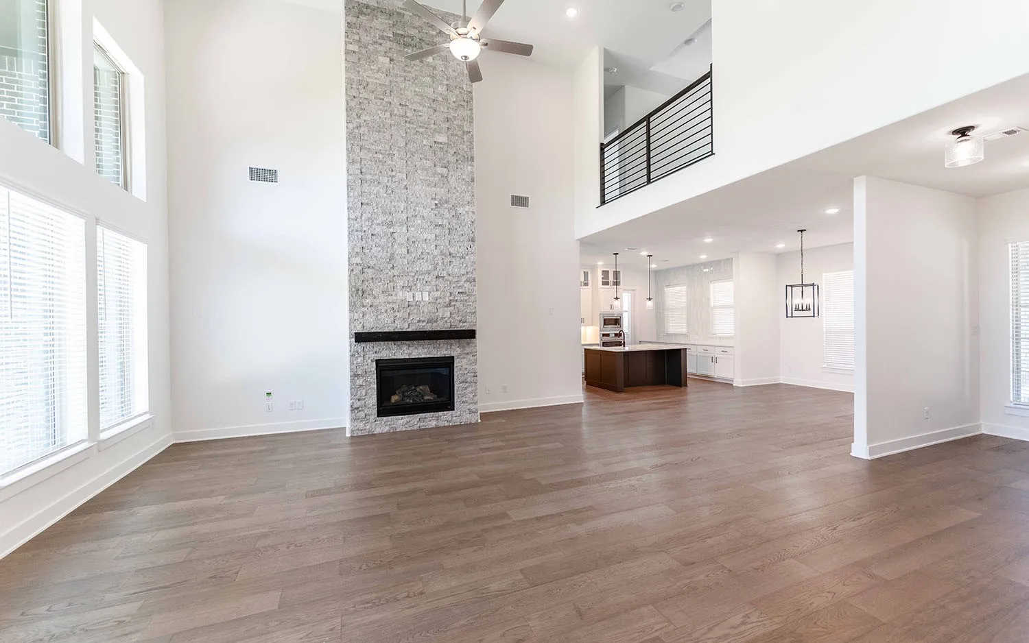 Expansive living space featuring high ceilings, wood-finish flooring, and a stone-clad fireplace with a dark wood mantel