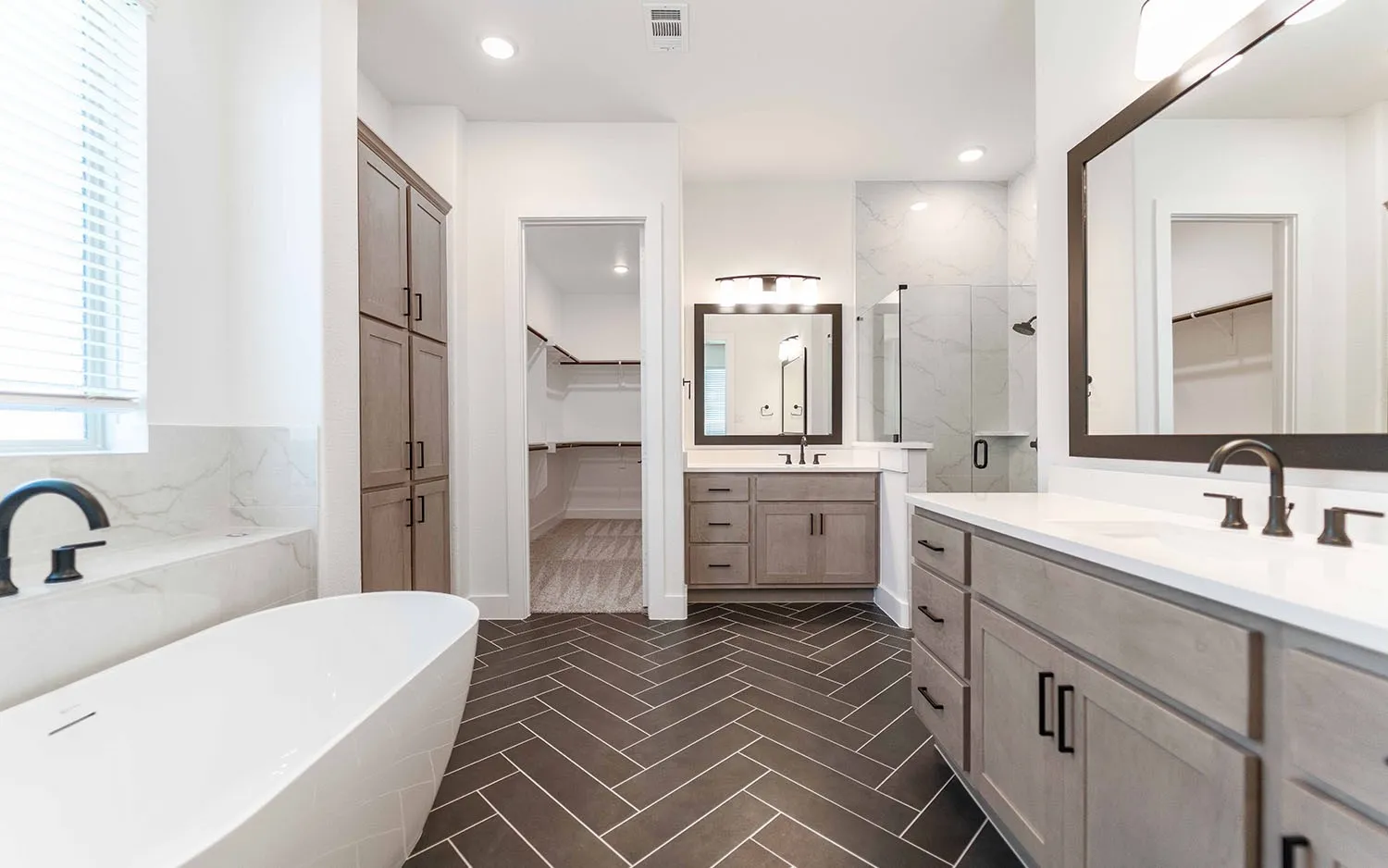Herringbone-patterned floor tiles complementing a freestanding soaking tub with a matte black faucet