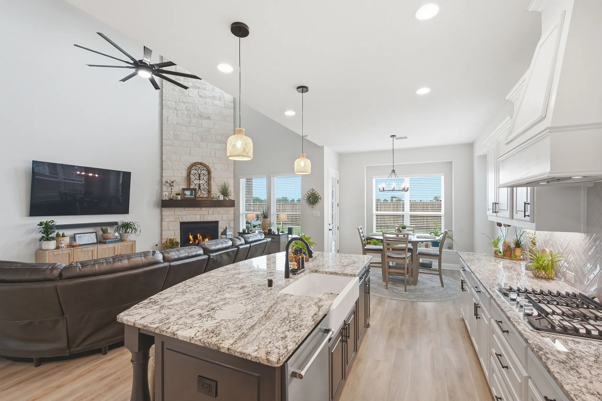 Open-concept living space featuring a central kitchen island with granite countertops and a farmhouse sink, stainless steel appliances, and wood-finish flooring