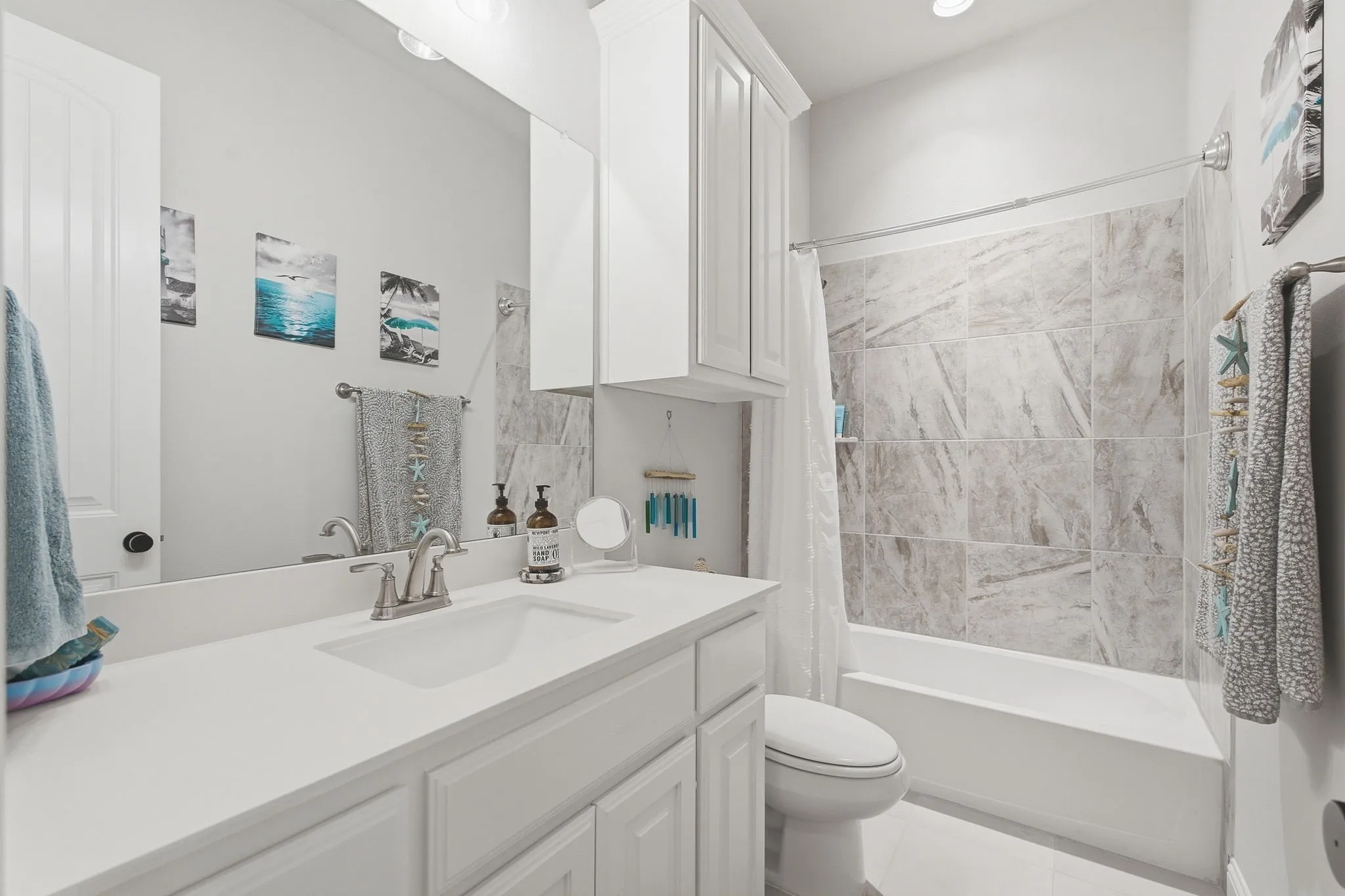 Bathroom featuring a vanity with white cabinetry, a single basin sink, a large wall mirror, and a tub with a tile surround