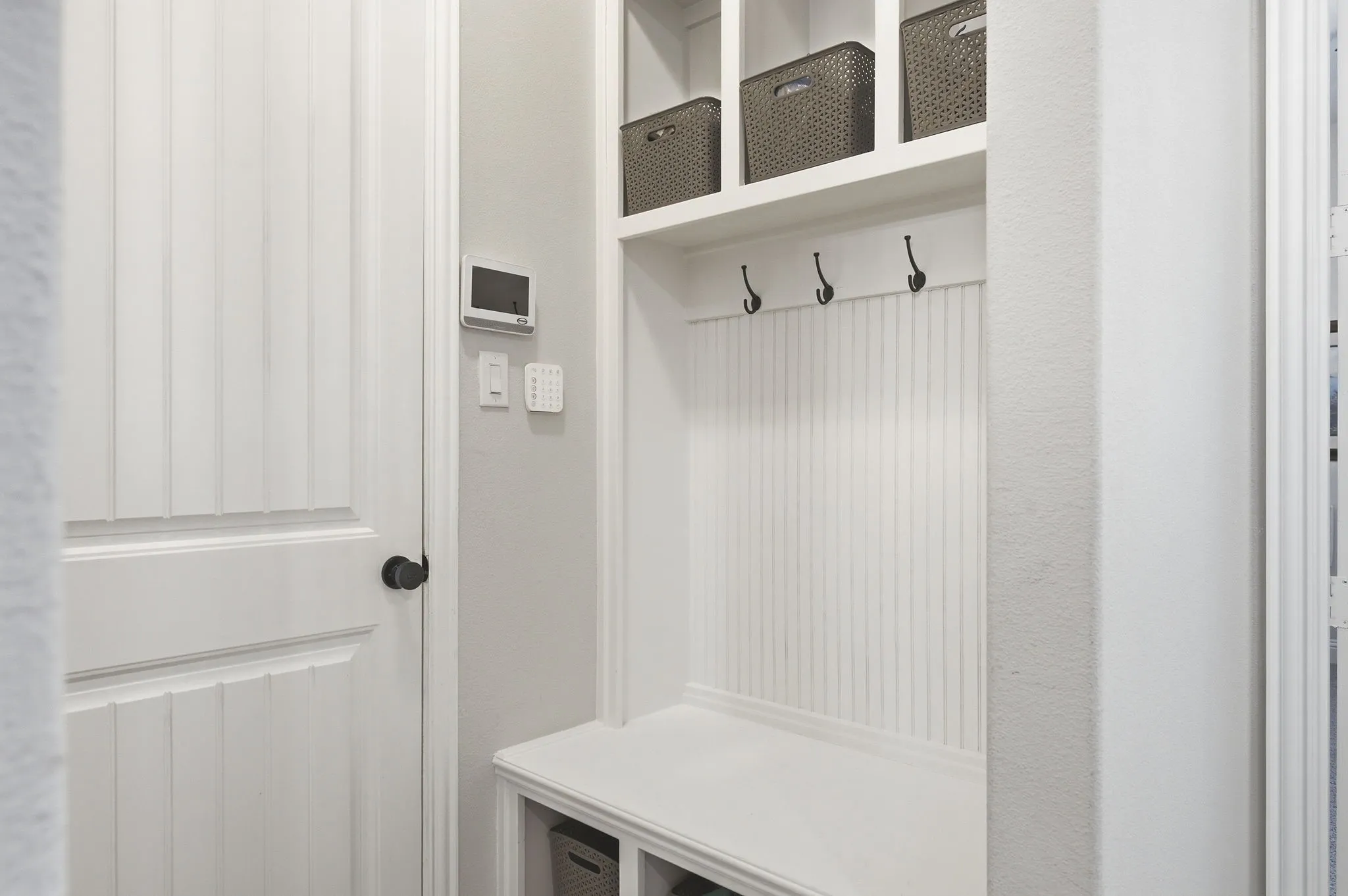 Built-in mudroom bench with three storage cubbies, three wall hooks, and beadboard paneling