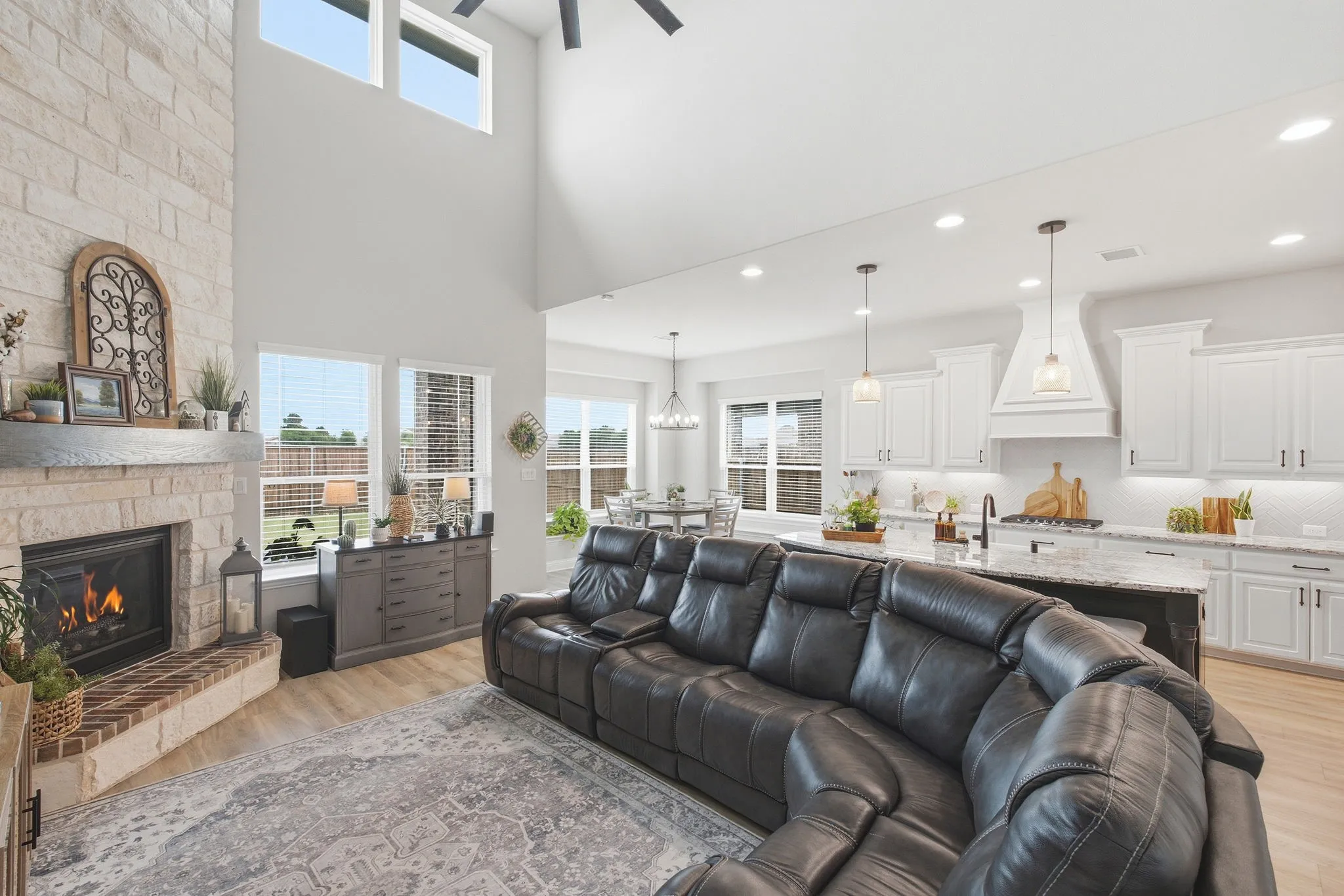 Two-story living area featuring a stone fireplace with a brick hearth, wood-finish flooring, and high windows