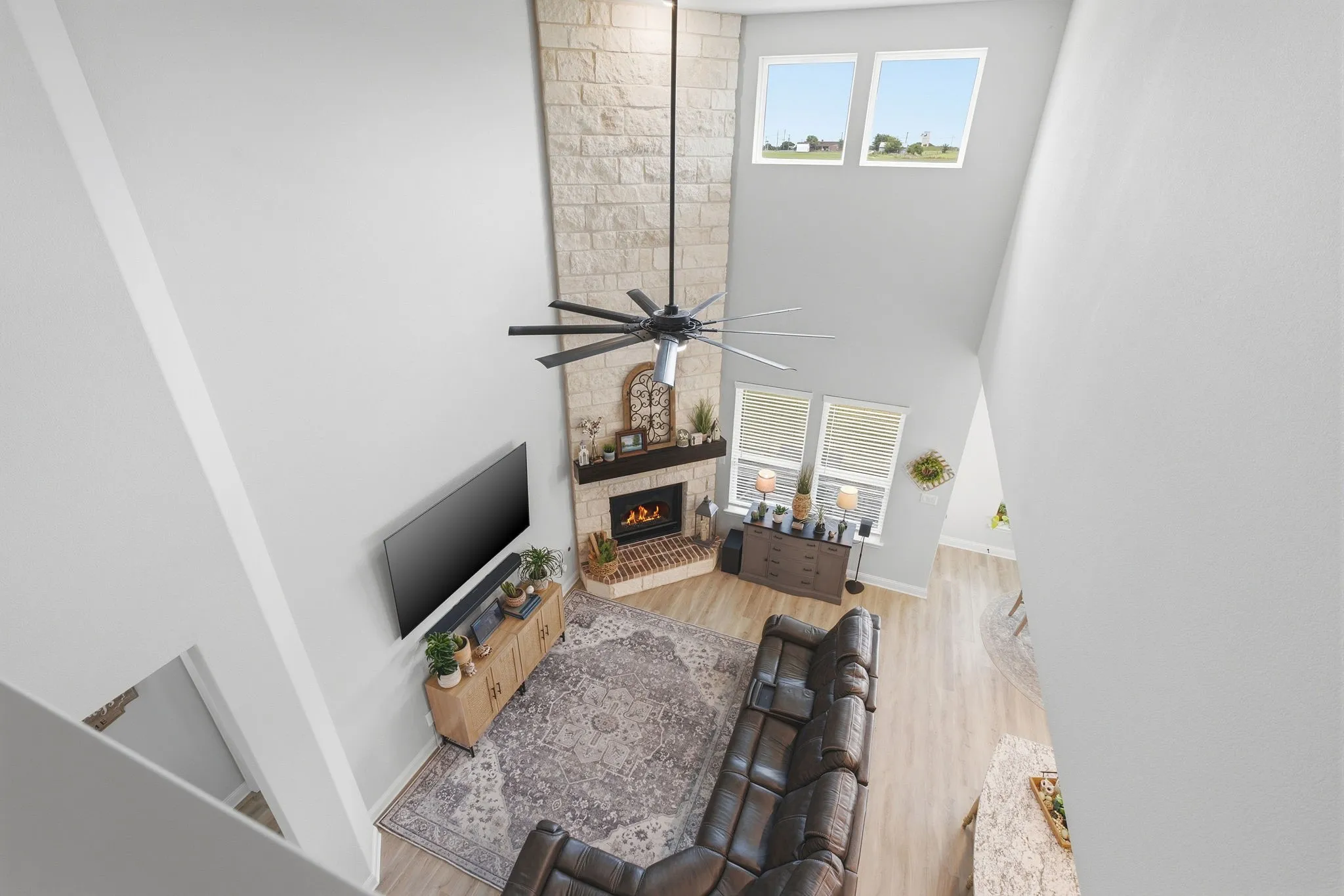 Two-story living area featuring a stone-clad fireplace with a dark wood mantel, high vaulted ceilings, and light wood-finish flooring