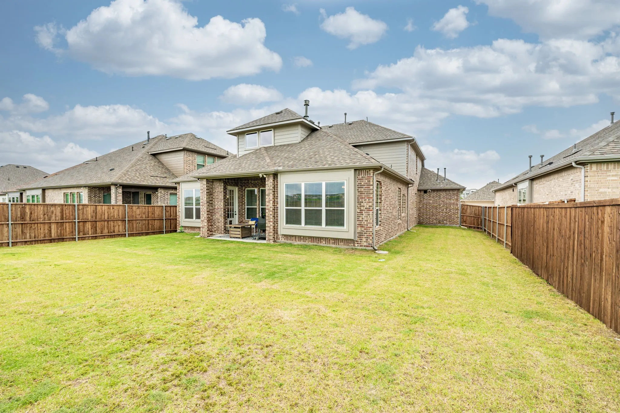 Expansive rear yard featuring a manicured lawn, full privacy fencing, and a covered patio area