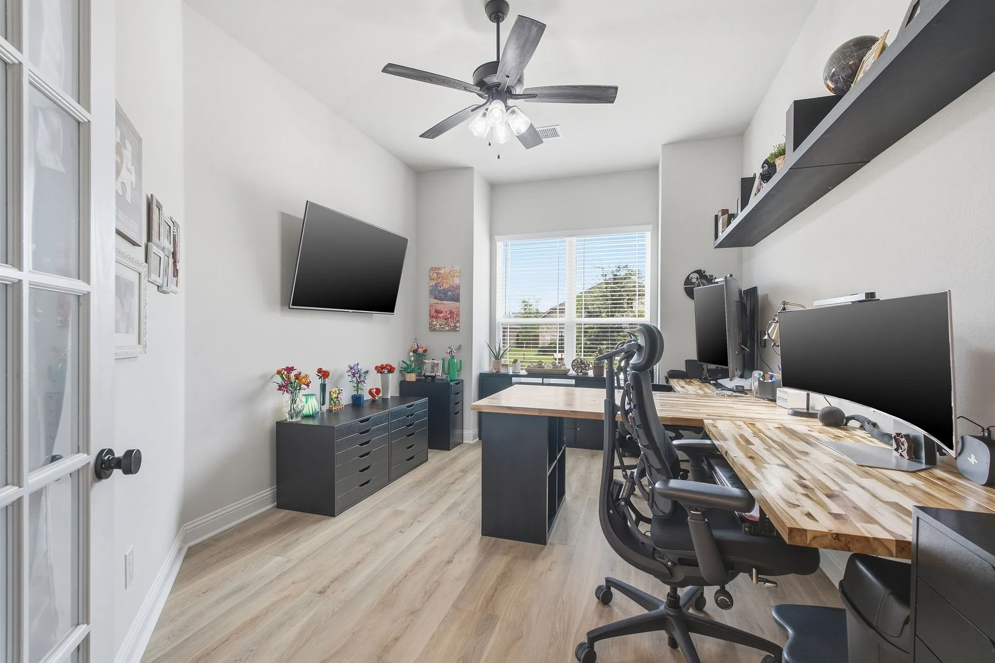 Dedicated office space featuring light wood-finish flooring, a ceiling fan, and large windows with blinds