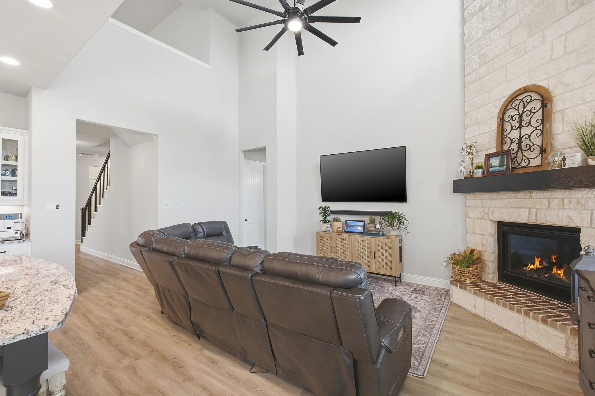 Living area featuring a high vaulted ceiling with a ceiling fan, a fireplace with a light-colored brick surround and a dark wood mantel, and wood-finish flooring