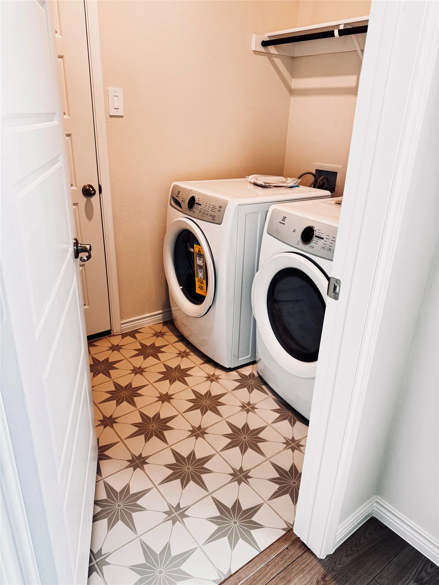 Laundry area featuring patterned tile flooring, a built-in shelf, and a hanging rod