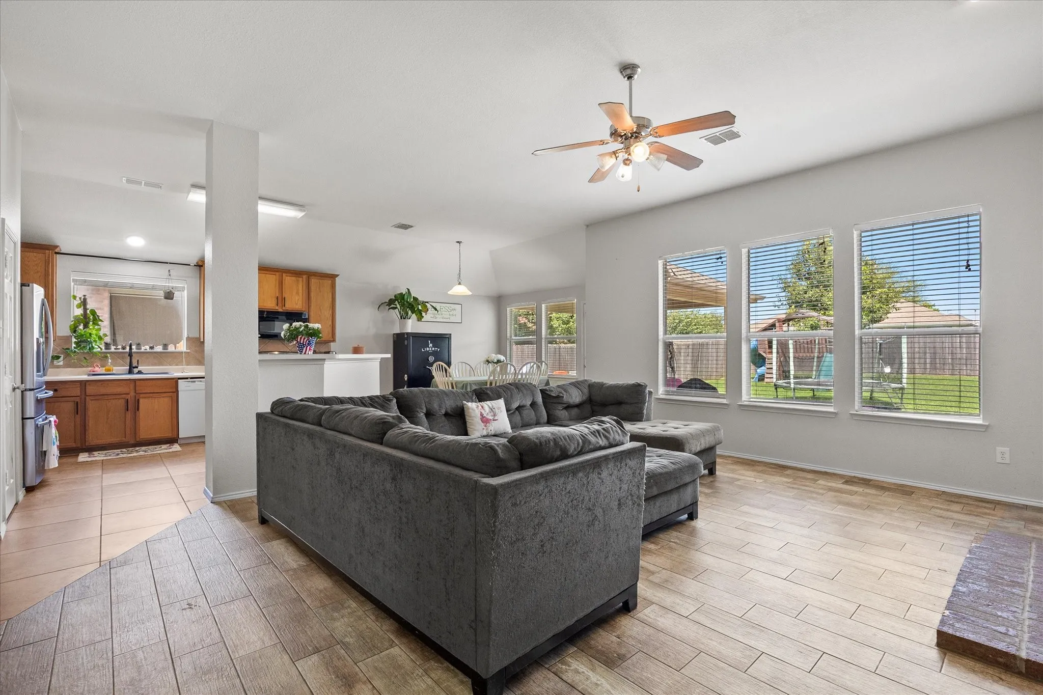 Spacious living area featuring wood-finish flooring, a ceiling fan, and multiple large windows with blinds