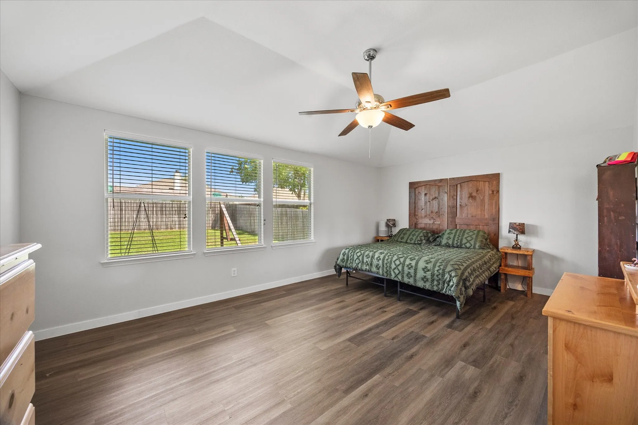 Spacious room featuring wood-finish flooring, a tray ceiling, and a ceiling fan with integrated lighting