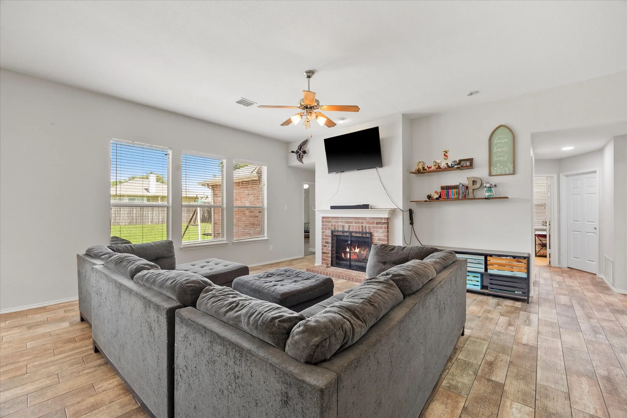 Spacious living area featuring a brick-surround fireplace, wood-finish flooring, and multiple windows with blinds