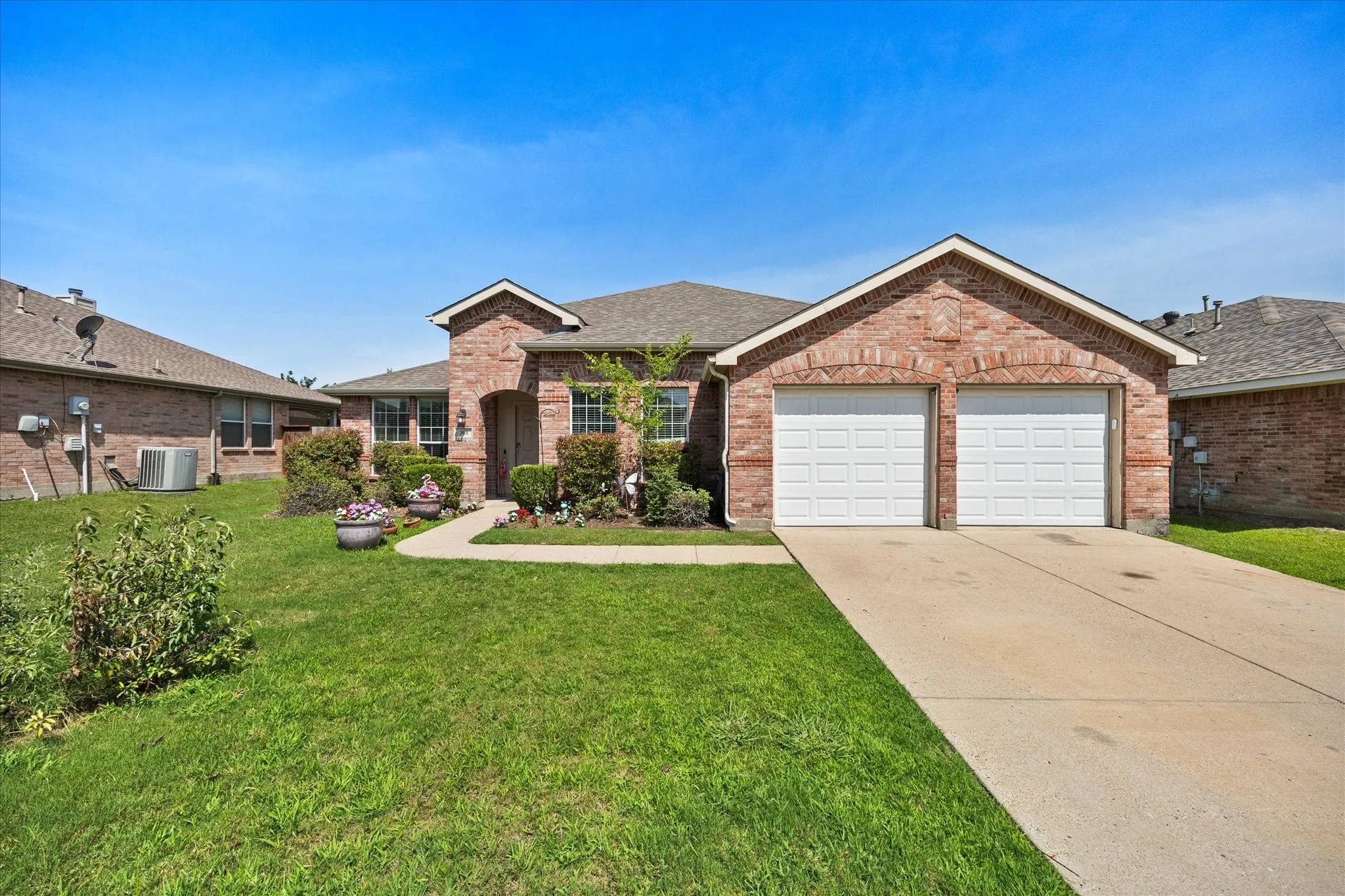 Brick exterior featuring a two-car garage with white panel doors, a concrete driveway, and a walkway leading to the front entry