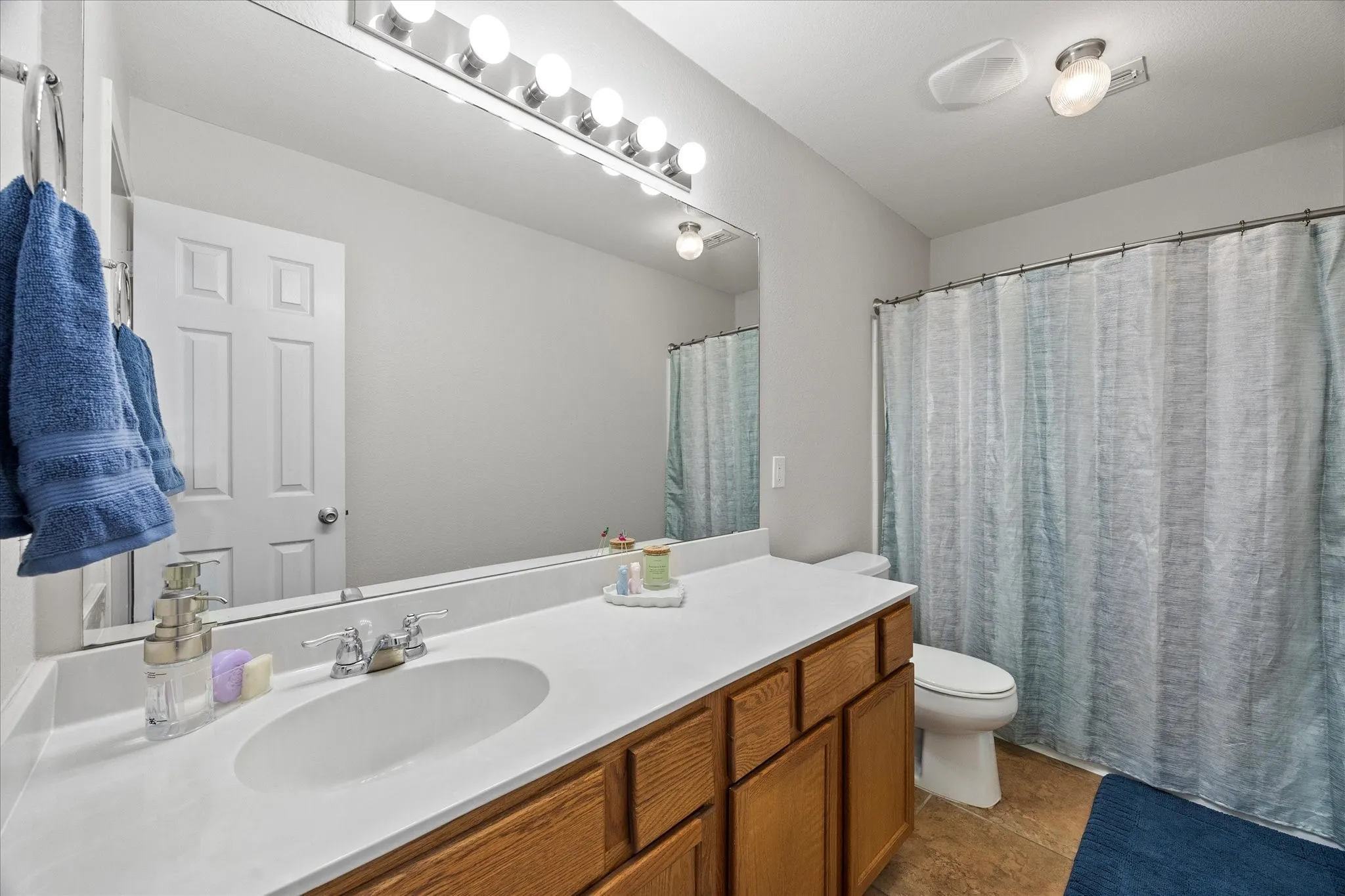 Bathroom featuring a wooden vanity with integrated sink, a large wall-mounted mirror, and a full shower/tub combination with a shower curtain