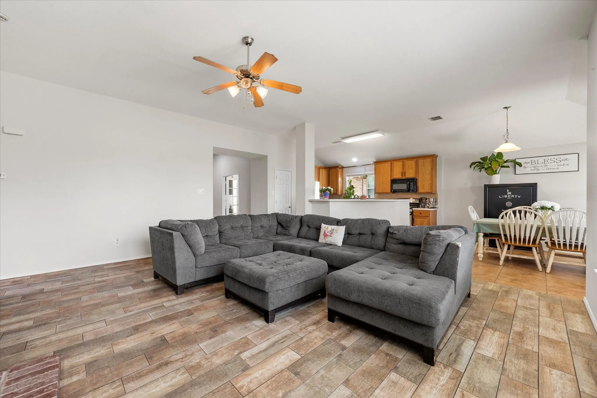 Open-concept living area featuring wood-finish flooring, a ceiling fan, and white walls
