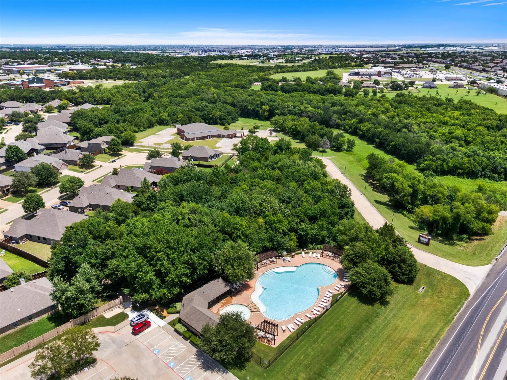 Community pool with surrounding lounge seating, adjacent clubhouse structure, and nearby paved parking