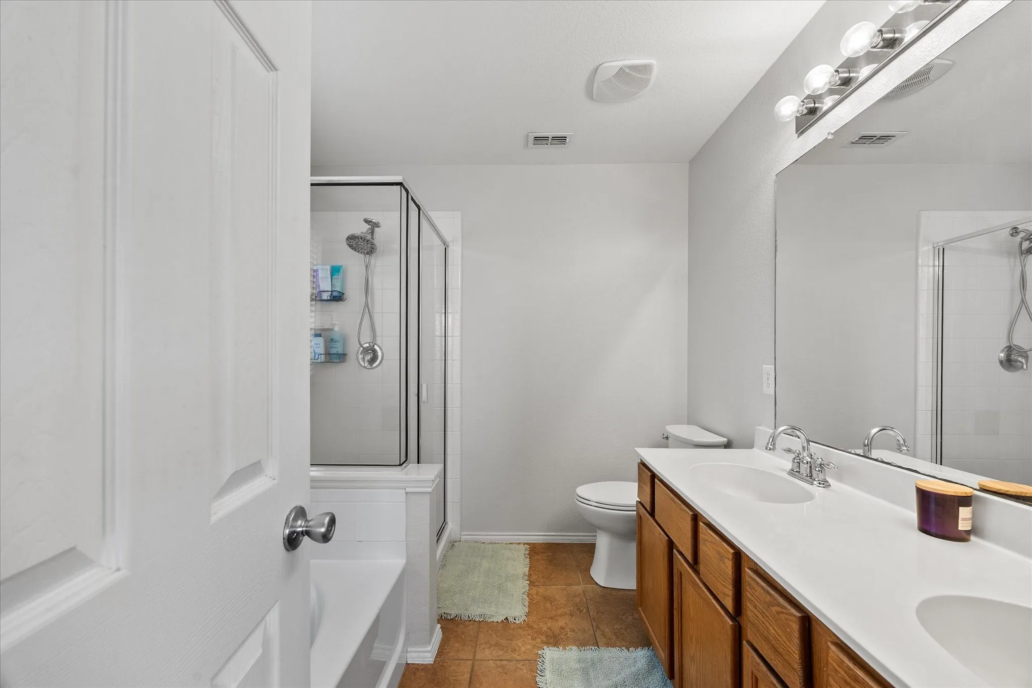 Bathroom featuring a dual-sink vanity with wood-finish cabinetry, a large mirror, and a glass-enclosed shower with a built-in bench