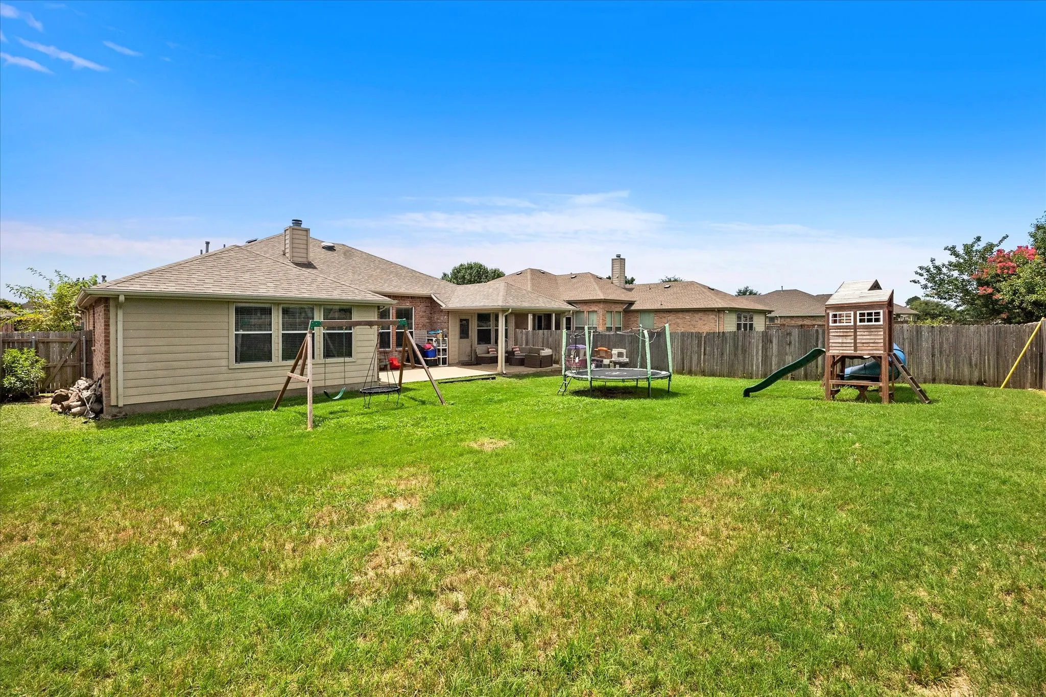 Expansive backyard featuring a manicured lawn, a full privacy fence, and a patio area