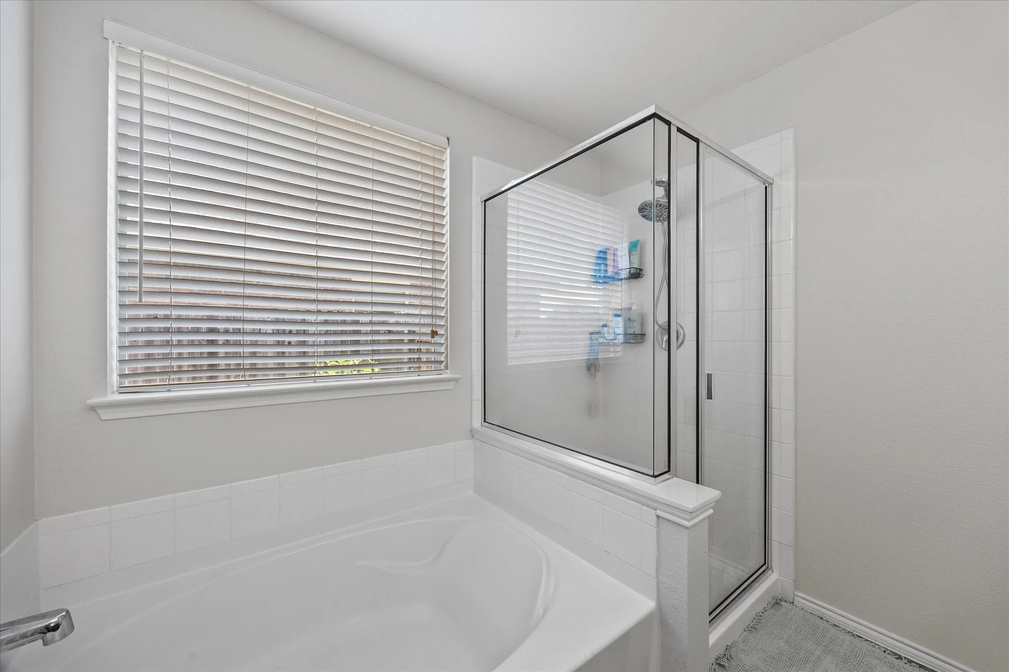 Soaking tub and glass-enclosed shower featuring white subway tile, chrome fixtures, and a large window with horizontal blinds