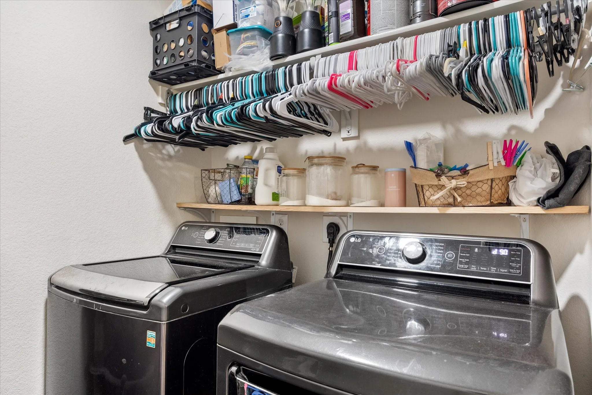Dedicated laundry space featuring a white wall finish, two appliances, a wooden shelf, and a white hanging rack