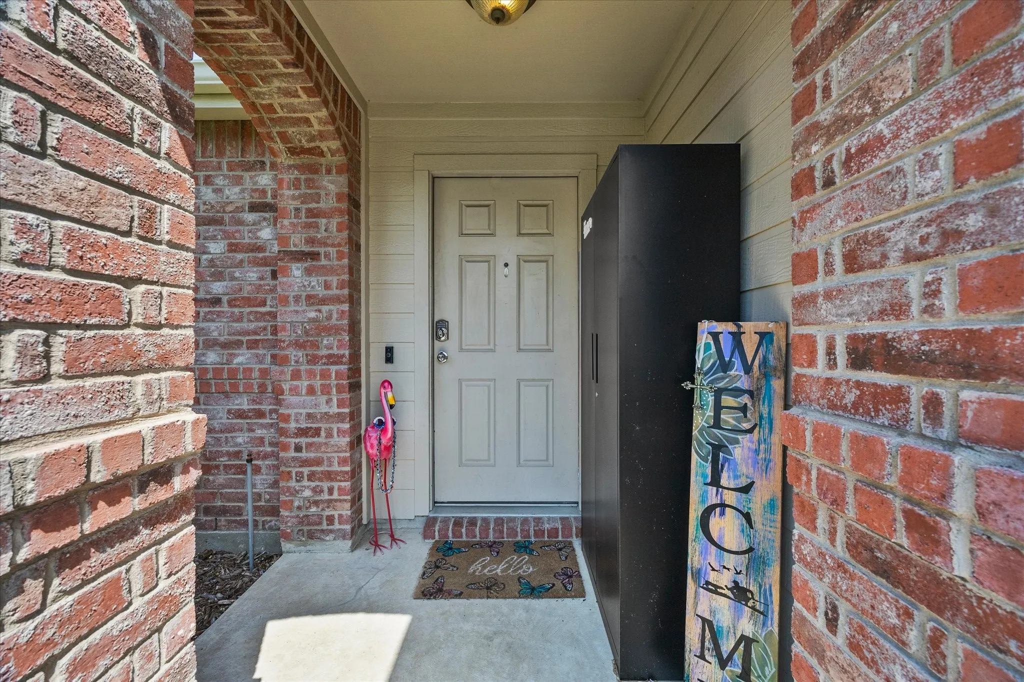 Entryway featuring a light-colored paneled door, red brick facade, and concrete porch