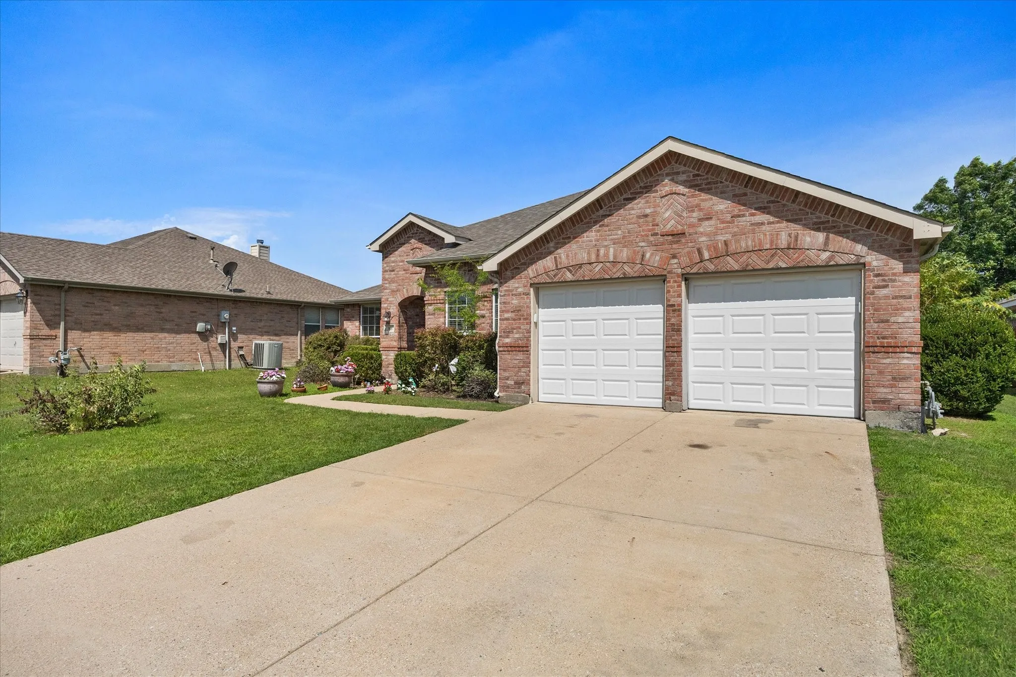 Brick exterior featuring a two-car garage with white paneled doors, an asphalt shingle roof, and a concrete driveway