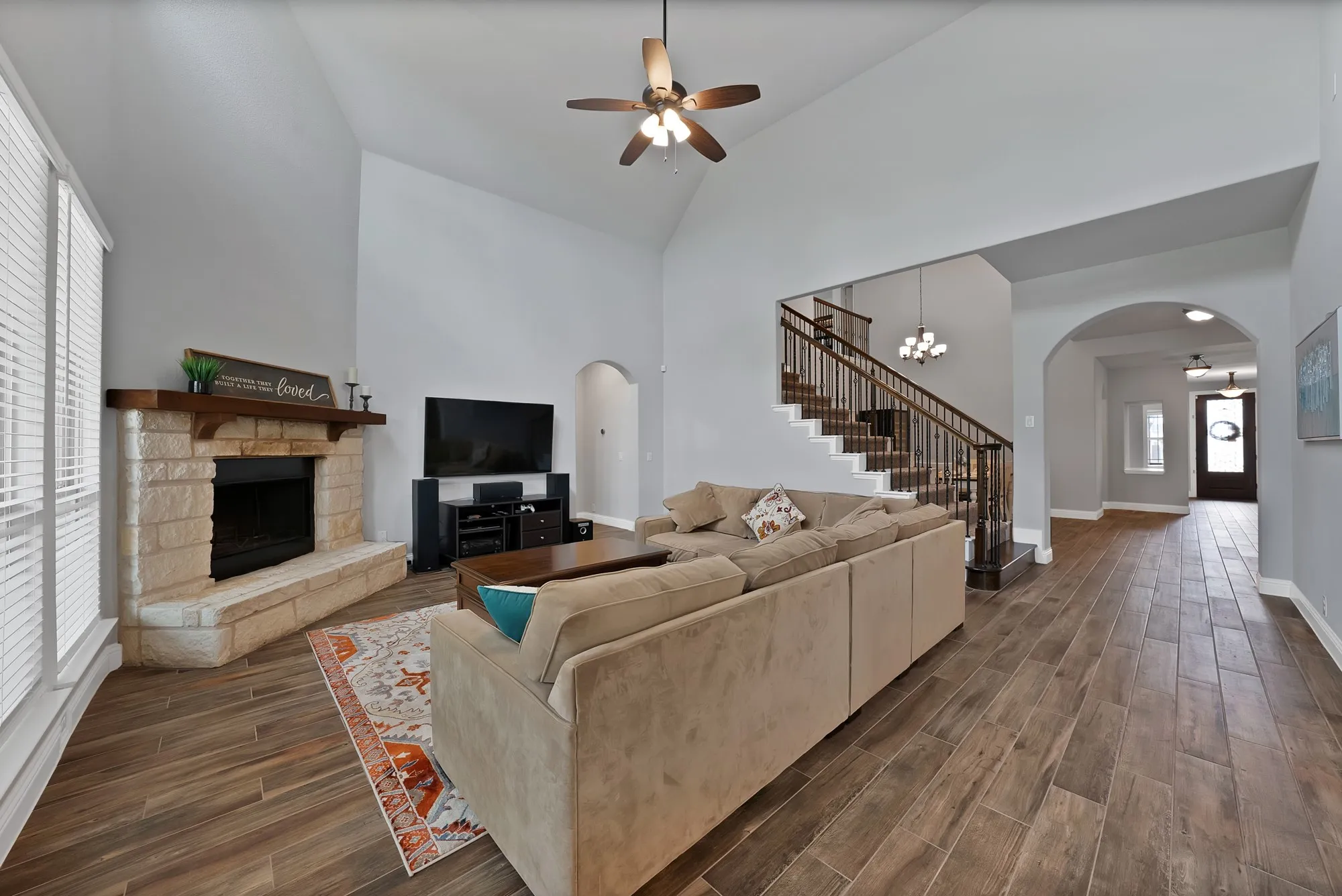 Spacious living area featuring high vaulted ceilings, wood-finish flooring, and a stone fireplace with a substantial wood mantle