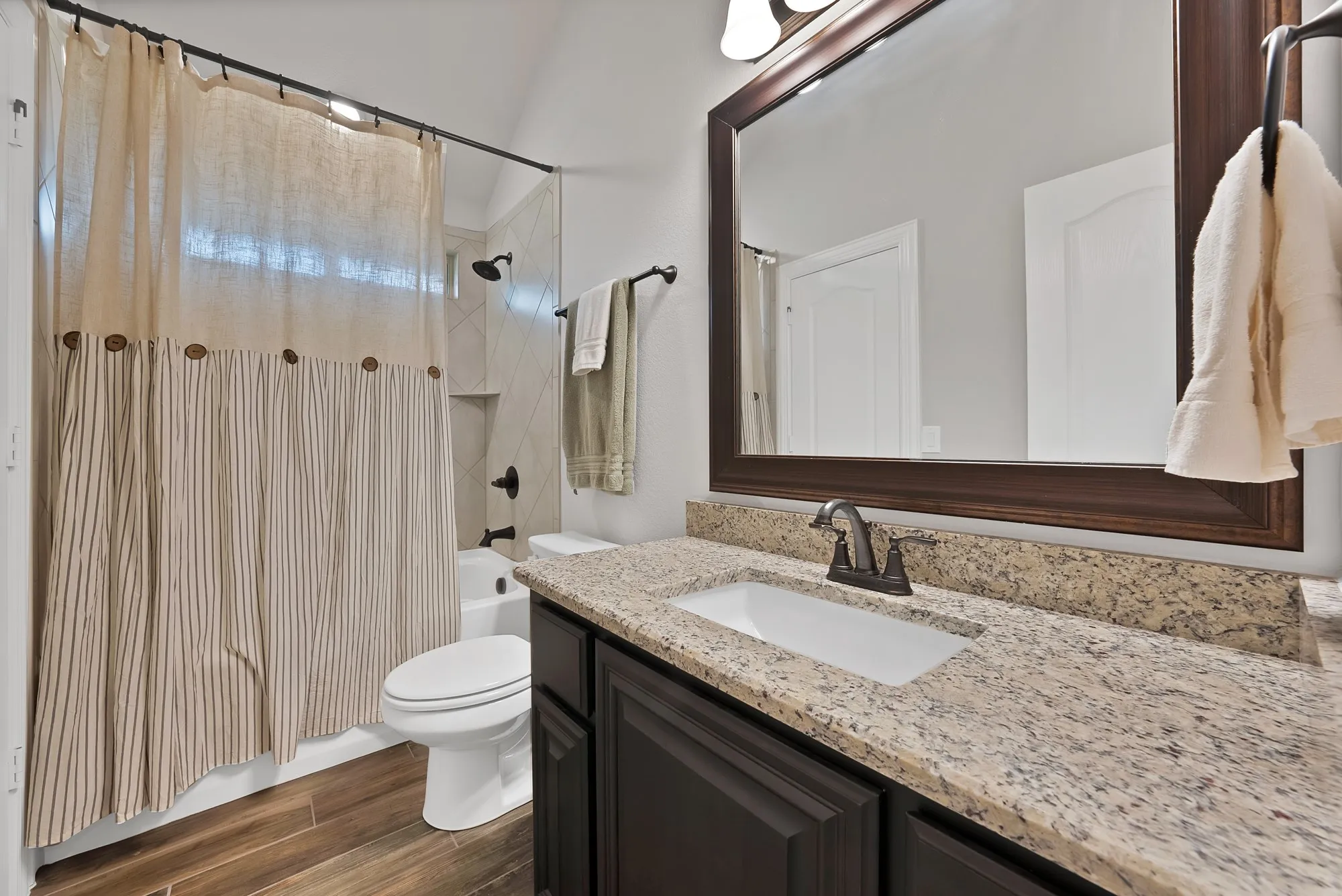 Bathroom featuring a granite countertop, undermount sink, dark wood-finish vanity, and a shower-tub combination with tiled surround and built-in niche