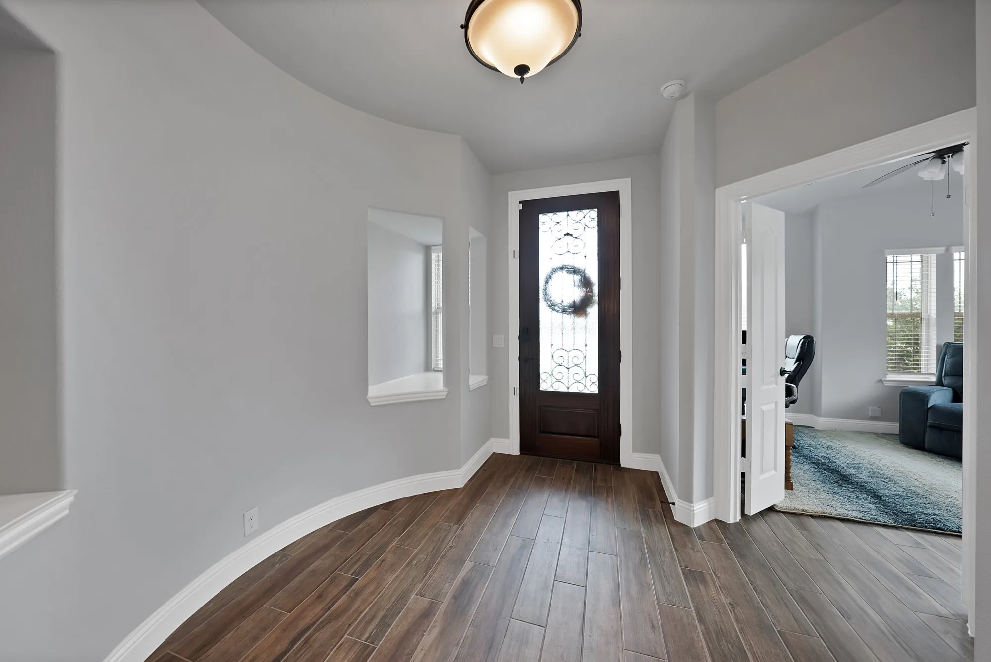 Entryway featuring wood-finish flooring, a dark wood front door with decorative glass, and a curved wall with display niches