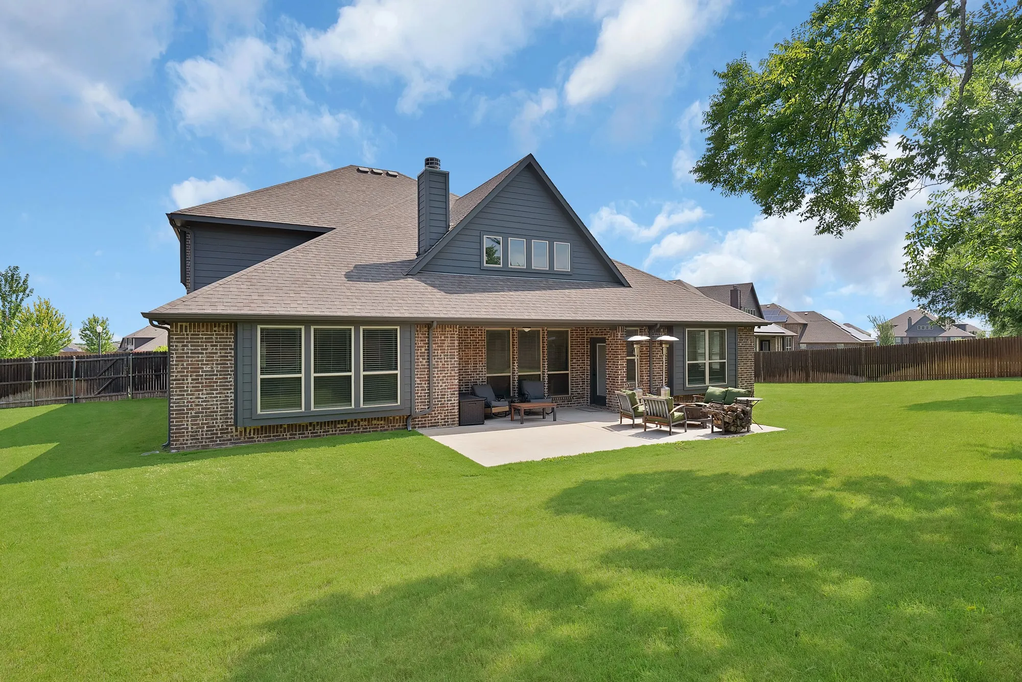 Expansive green lawn surrounds a rear elevation featuring a covered patio and a concrete patio space
