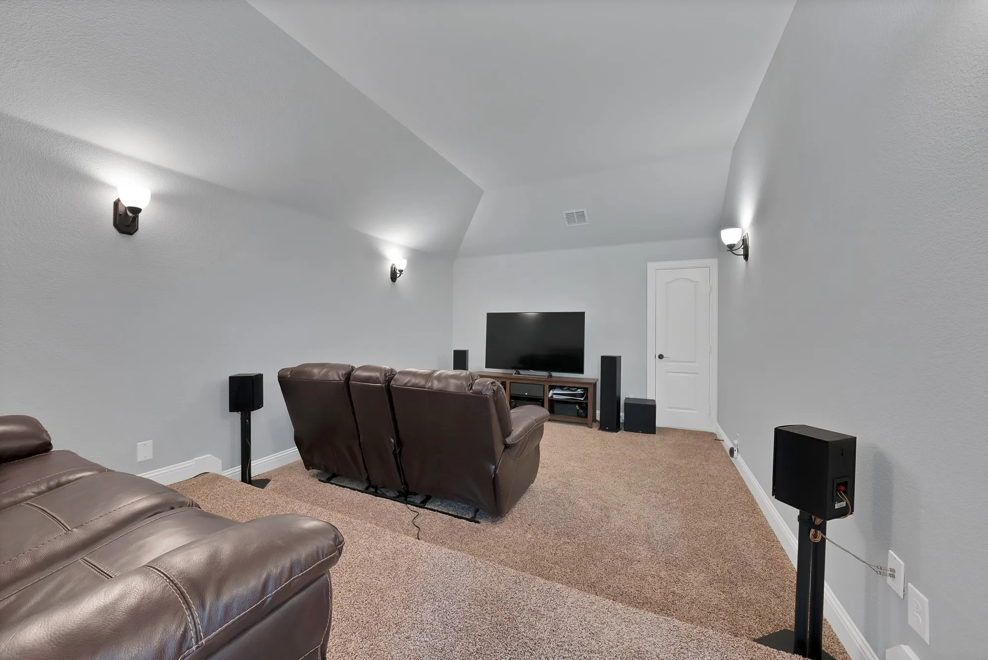 Carpeted media room featuring sloped ceilings, wall sconces, a built-in media console, and a paneled interior door