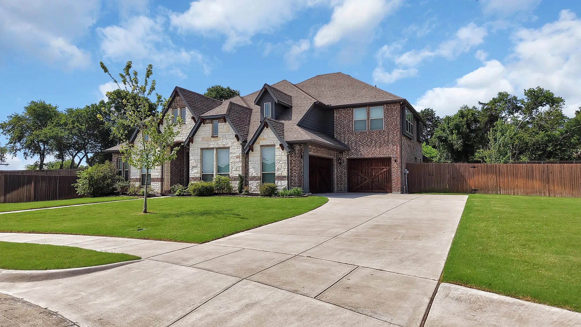 Two-story residence featuring a brick and stone facade, a multi-gabled roofline, and a concrete driveway