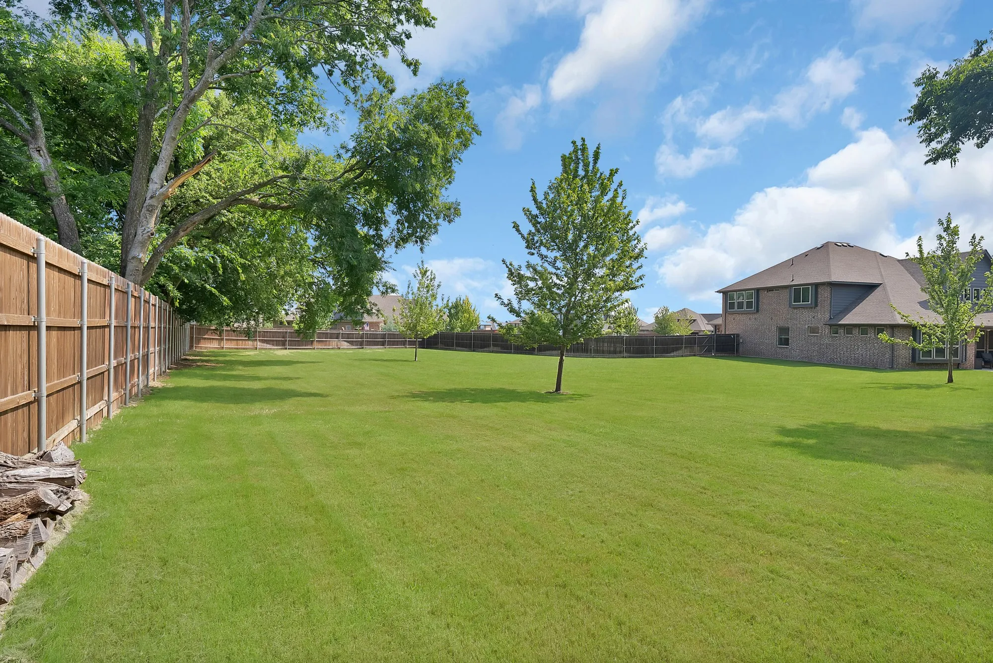 Expansive green lawn with mature trees and a privacy fence