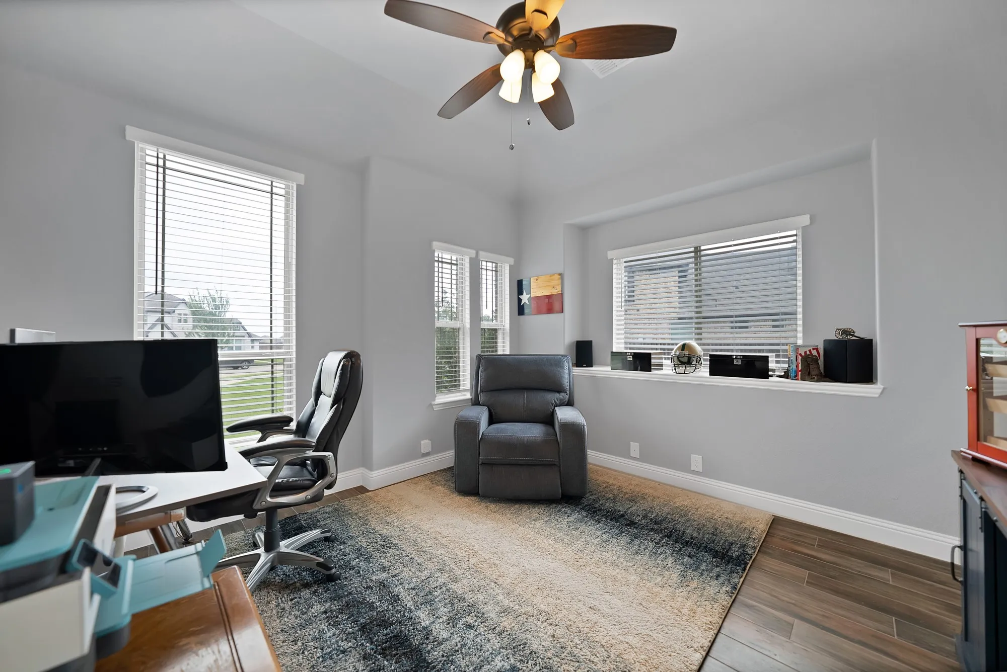 Spacious room featuring multiple windows with blinds, light gray wall paint, and wood-finish flooring