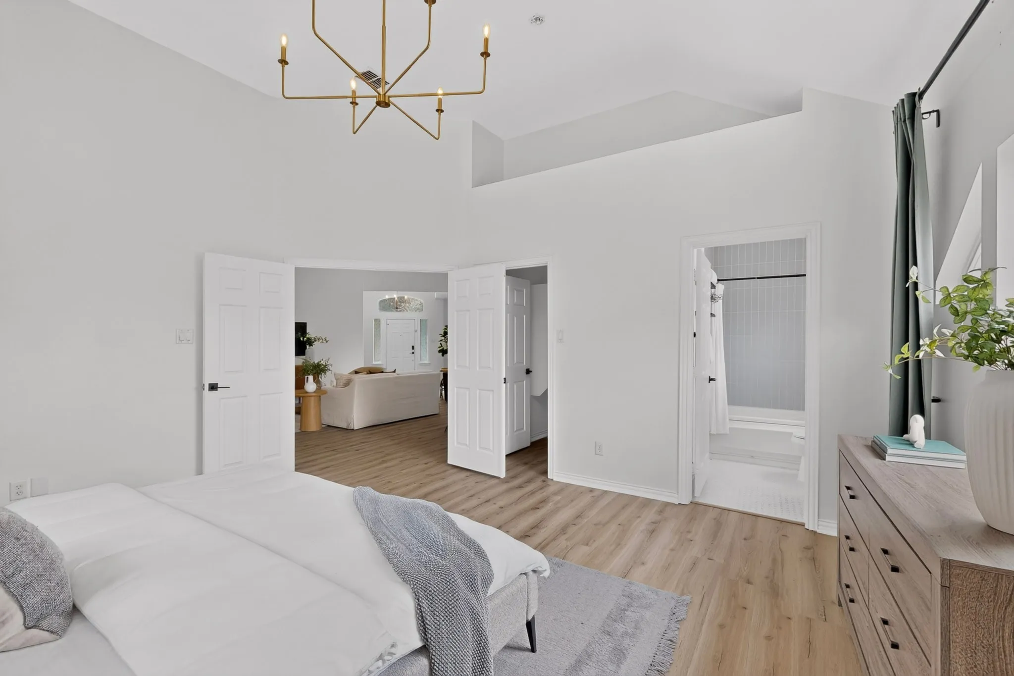Vaulted ceilings with a prominent brass chandelier, wood-finish flooring, and a light color palette