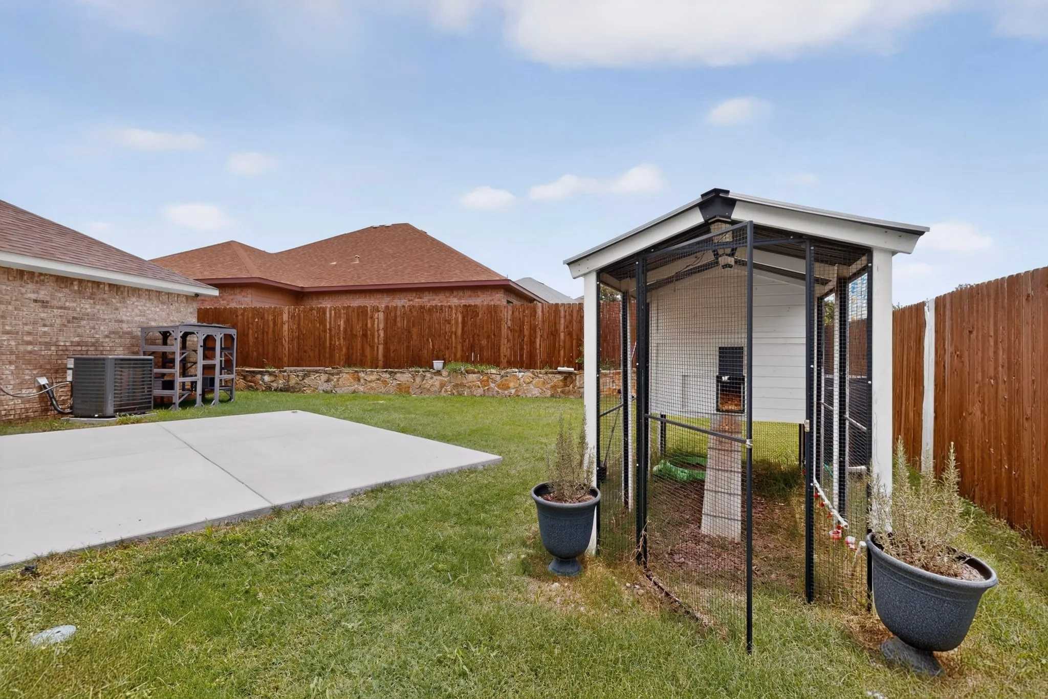 Expansive backyard featuring a concrete patio, a wooden privacy fence, and a dedicated animal enclosure