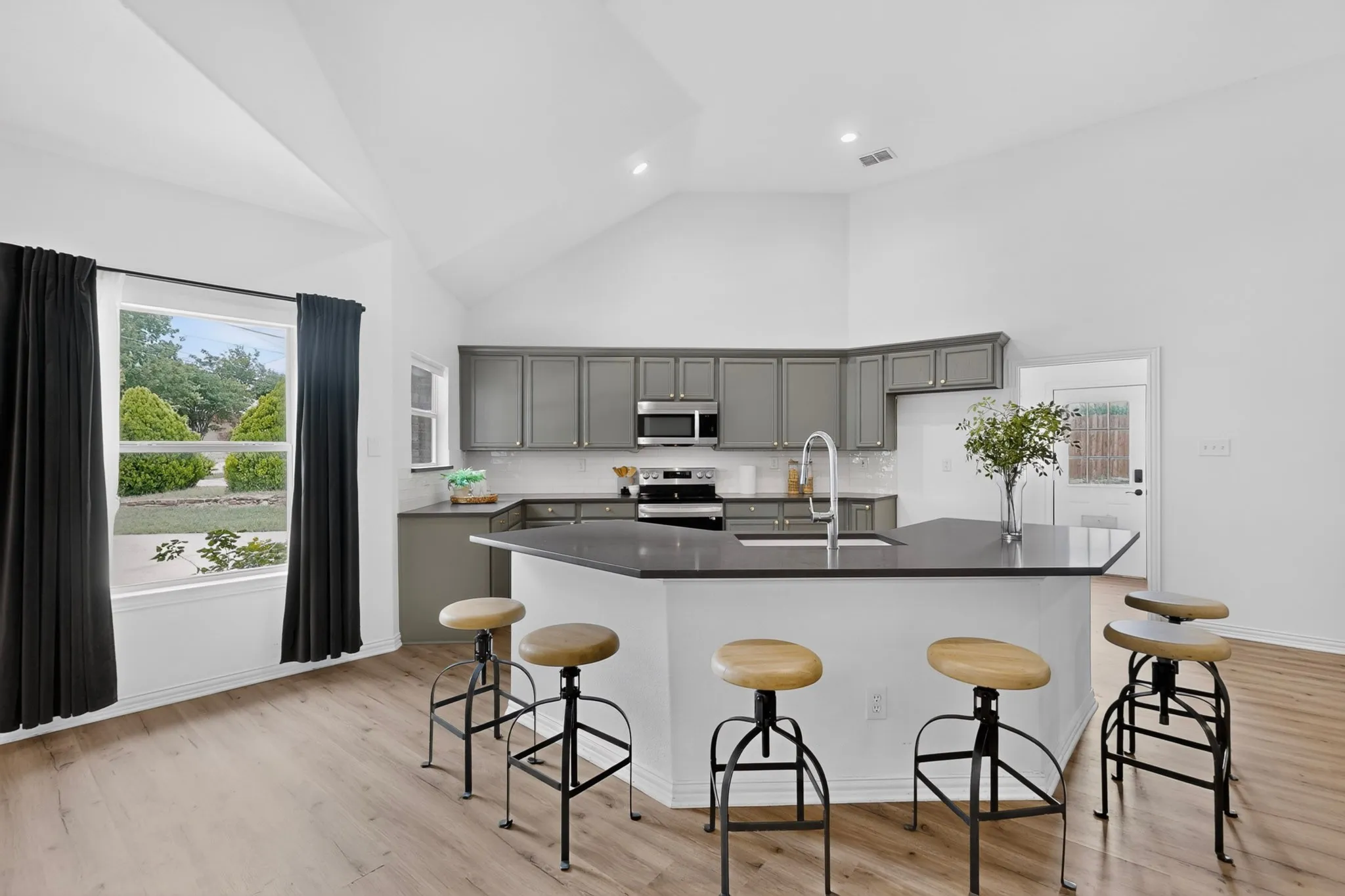 Kitchen featuring a large island with countertop seating, stainless steel appliances, grey cabinetry, and wood-finish flooring