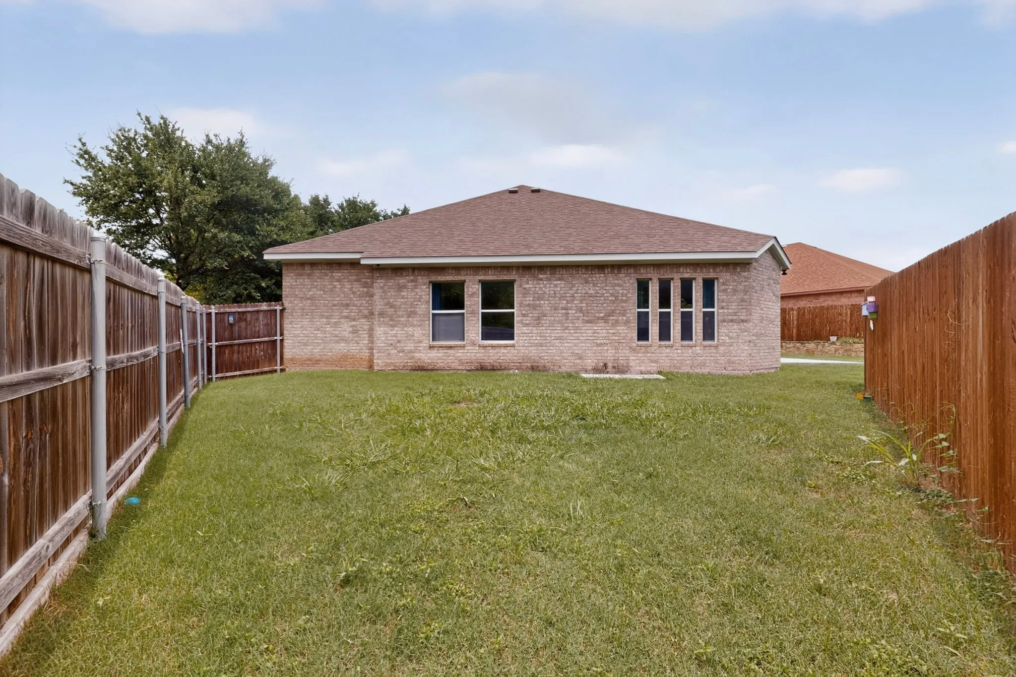 Fenced backyard featuring a brick exterior, multiple windows, and a shingle roof