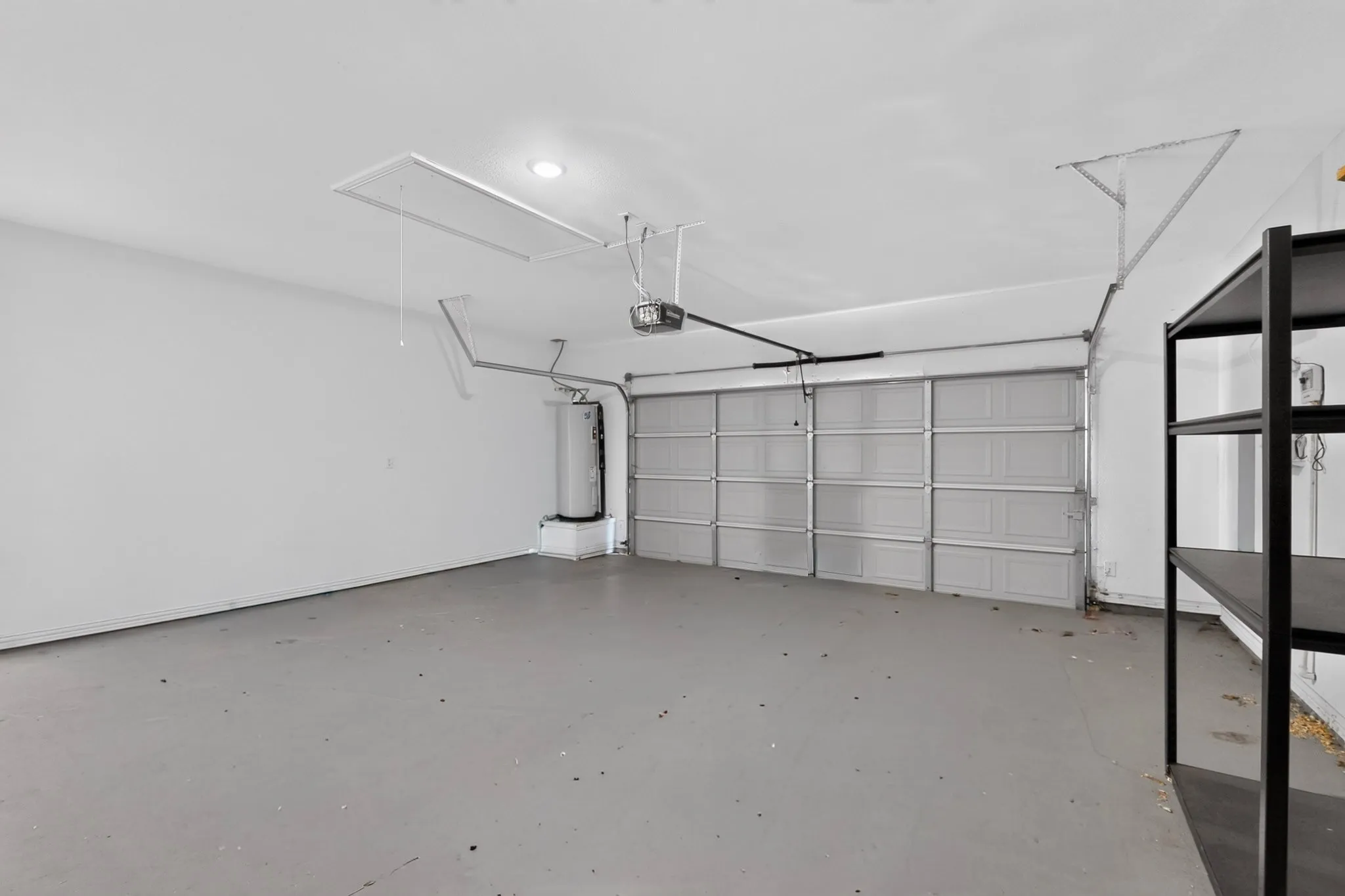 Spacious garage featuring a sectional garage door, exposed water heater, and built-in shelving