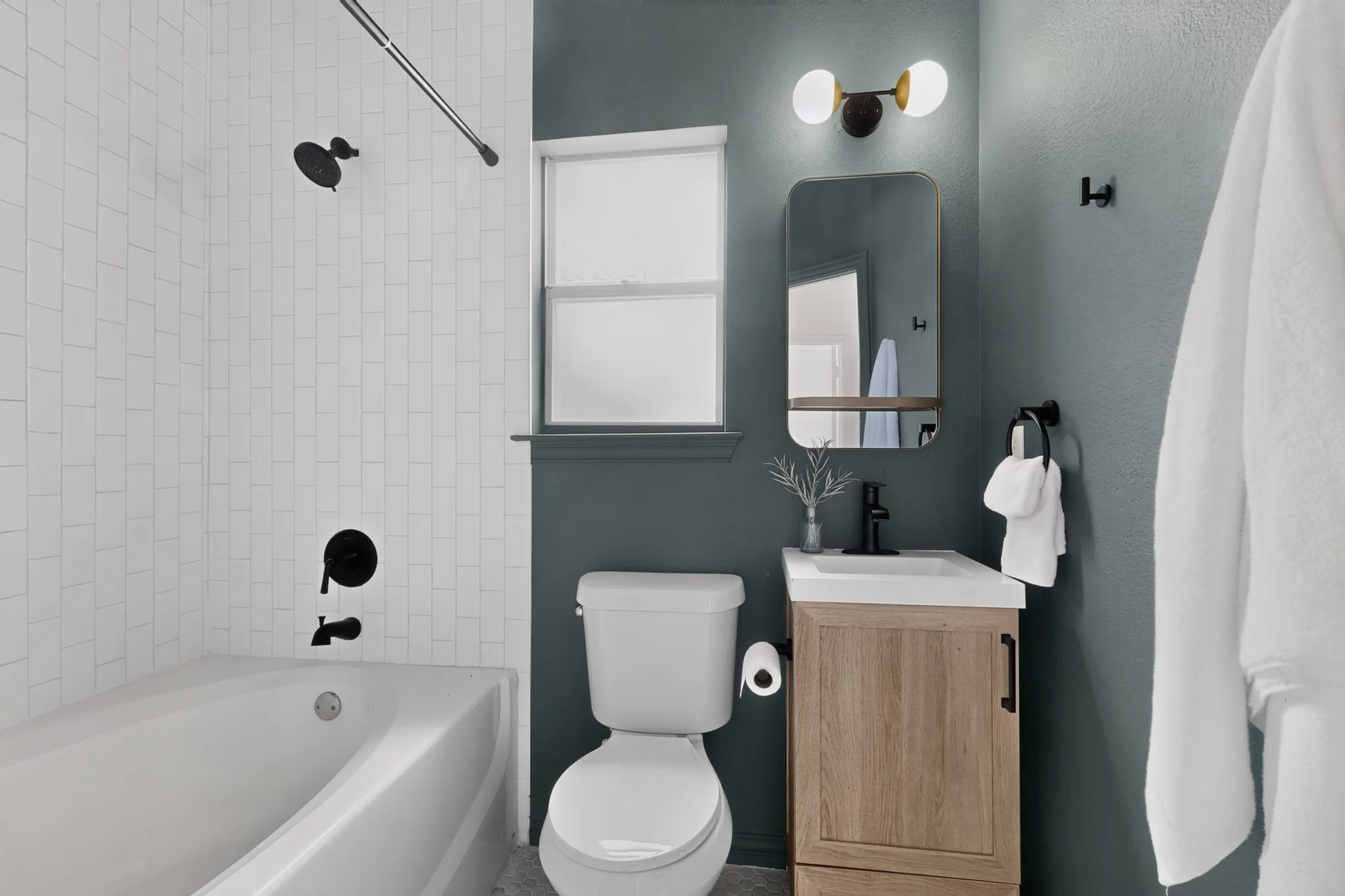 Bathroom featuring a white subway tile shower surround, matte black fixtures, a single vanity with wood-finish cabinetry, white countertop, and a contemporary wall-mounted light fixture