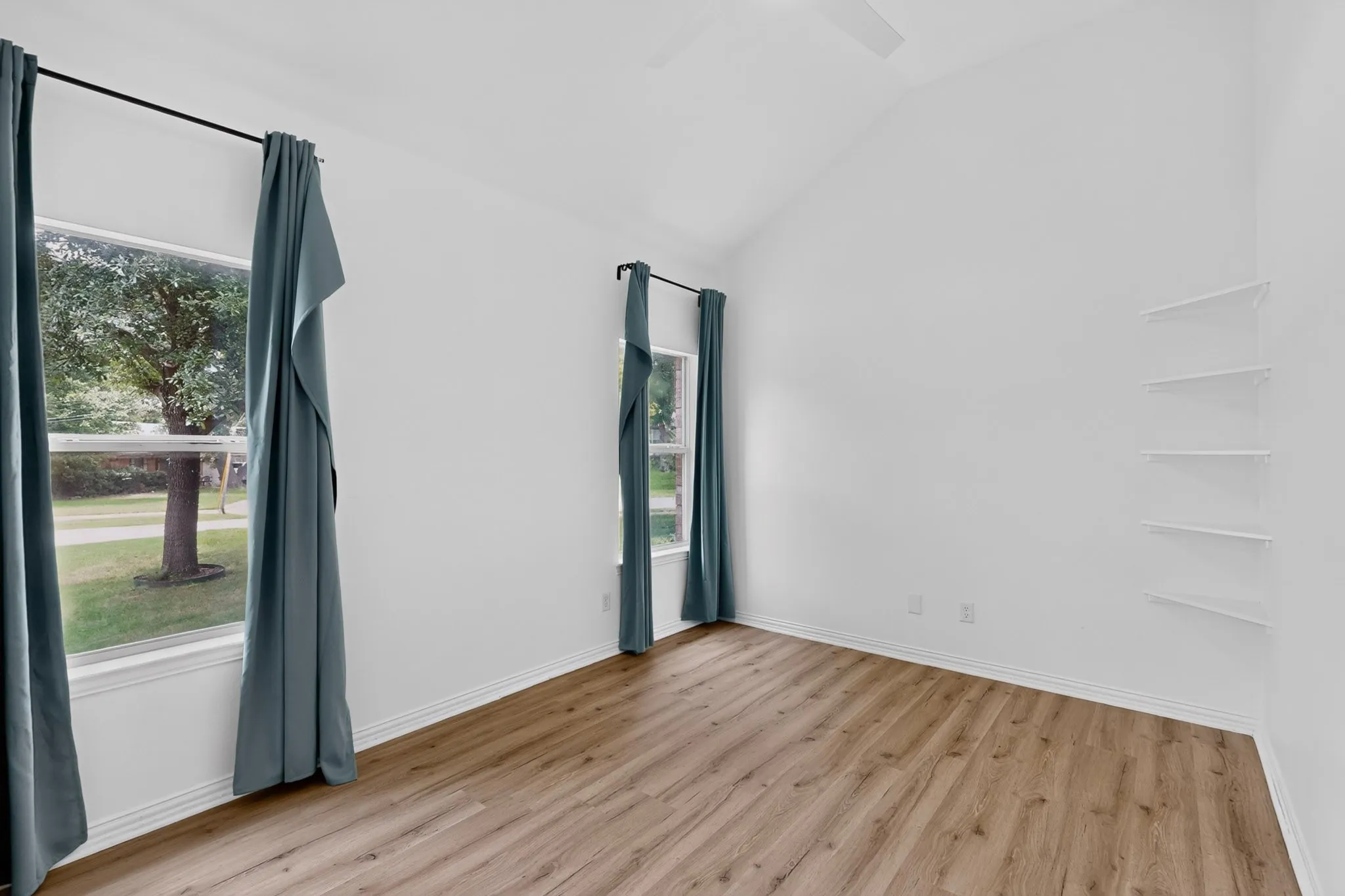 Vaulted ceiling bedroom featuring wood-finish flooring, multiple windows, and built-in wall shelving