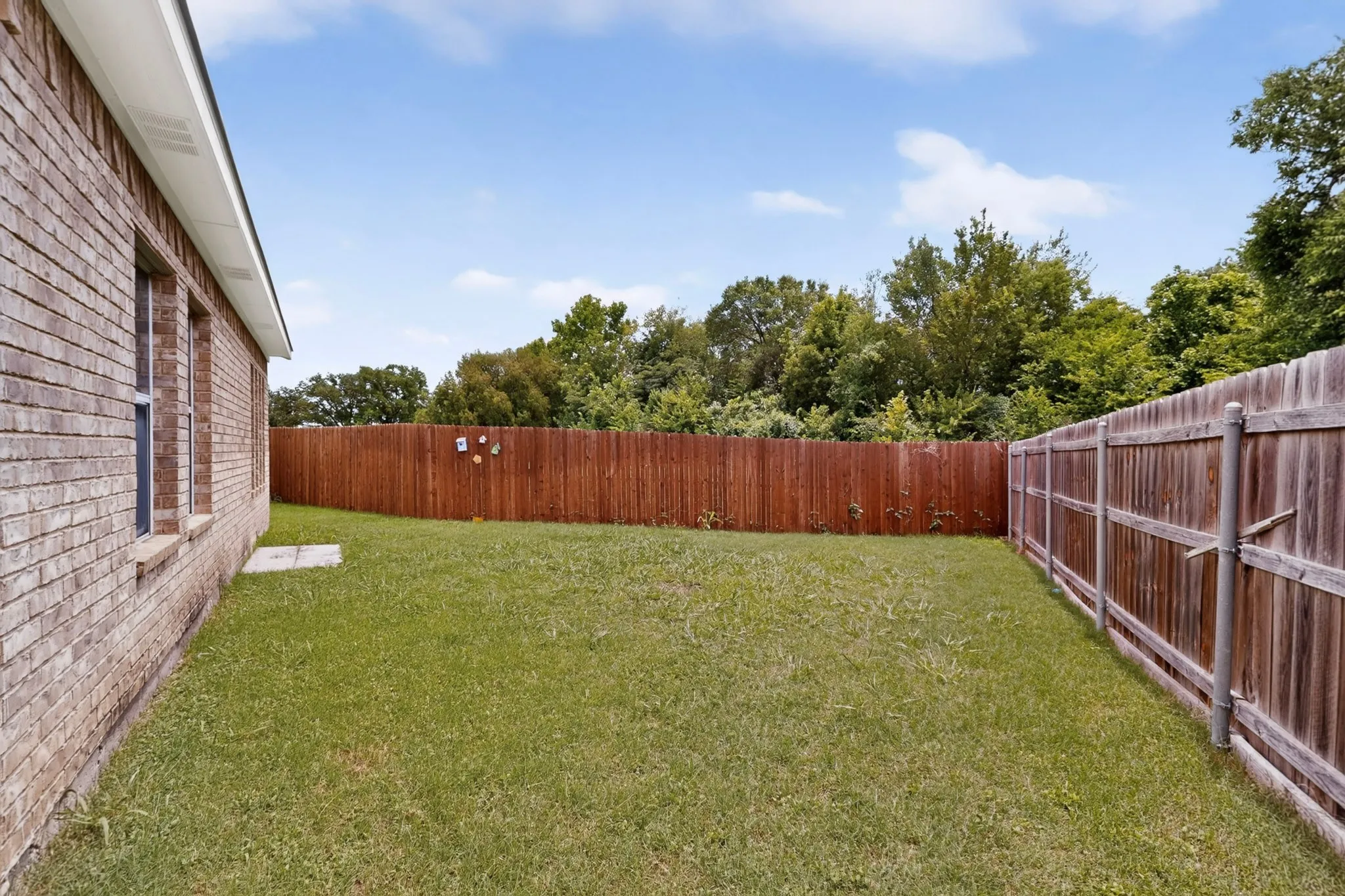 Expansive backyard featuring a manicured lawn, a wood privacy fence, and a brick exterior wall with multiple windows
