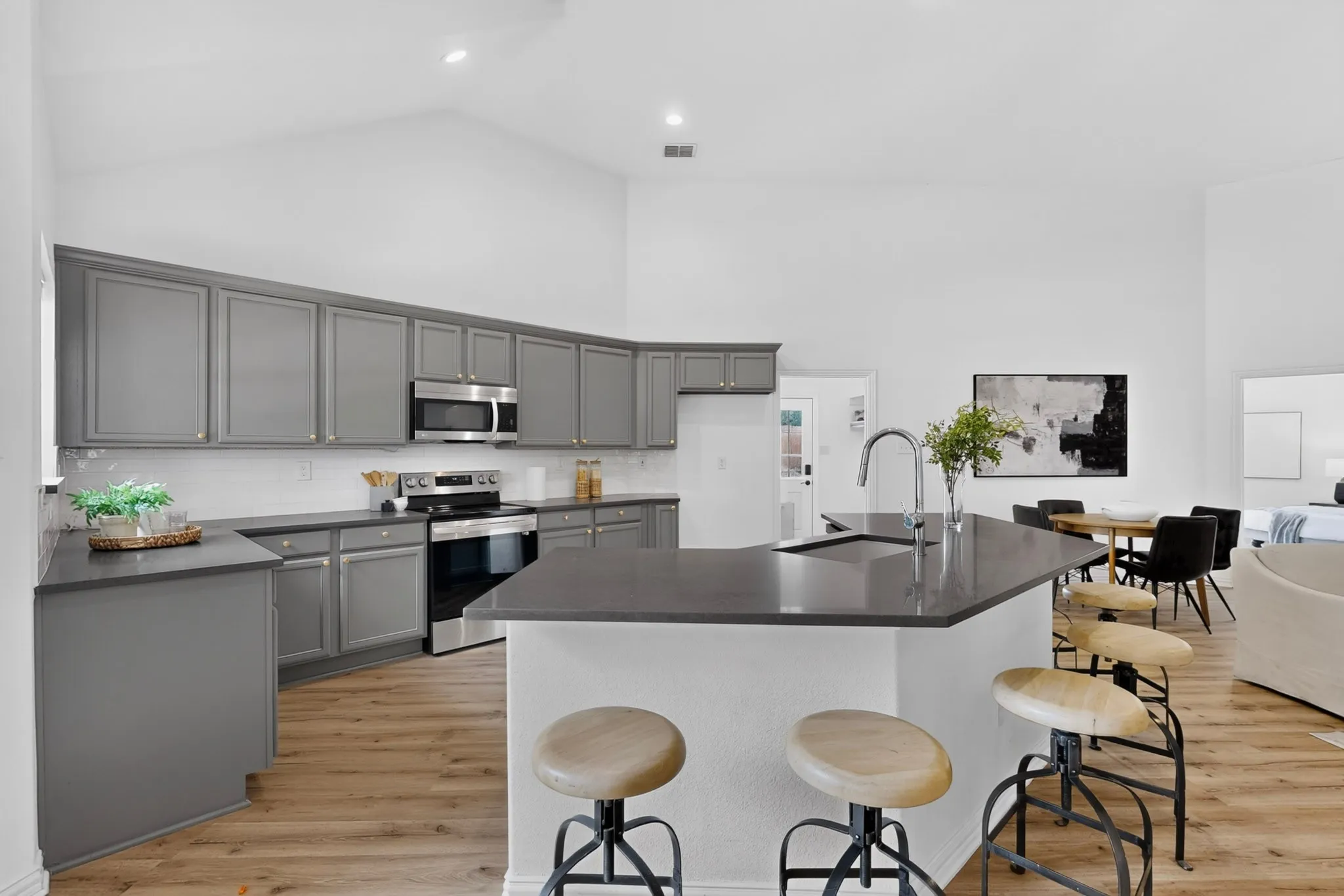 Open-concept kitchen featuring gray cabinetry, stainless steel appliances, a center island with a sink, and wood-finish flooring