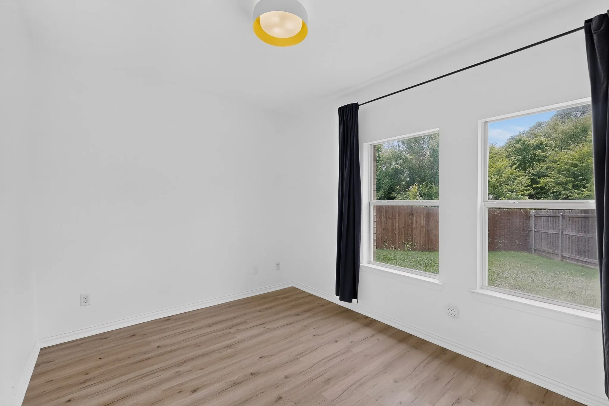 Room featuring two large windows with backyard views, wood-finish flooring, and a modern flush-mount ceiling light
